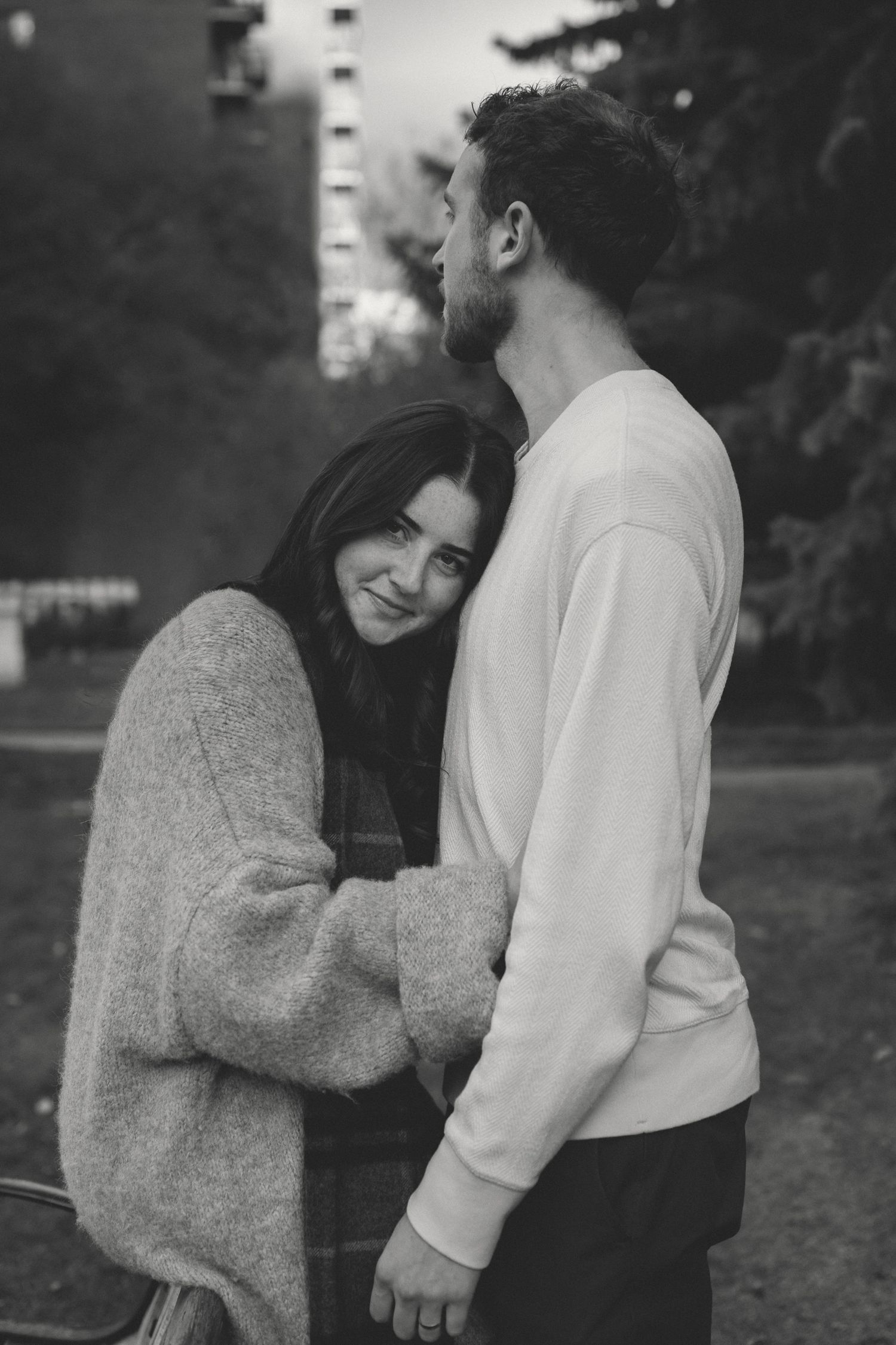 A romantic black and white photo of a couple embracing outdoors in casual sweaters.