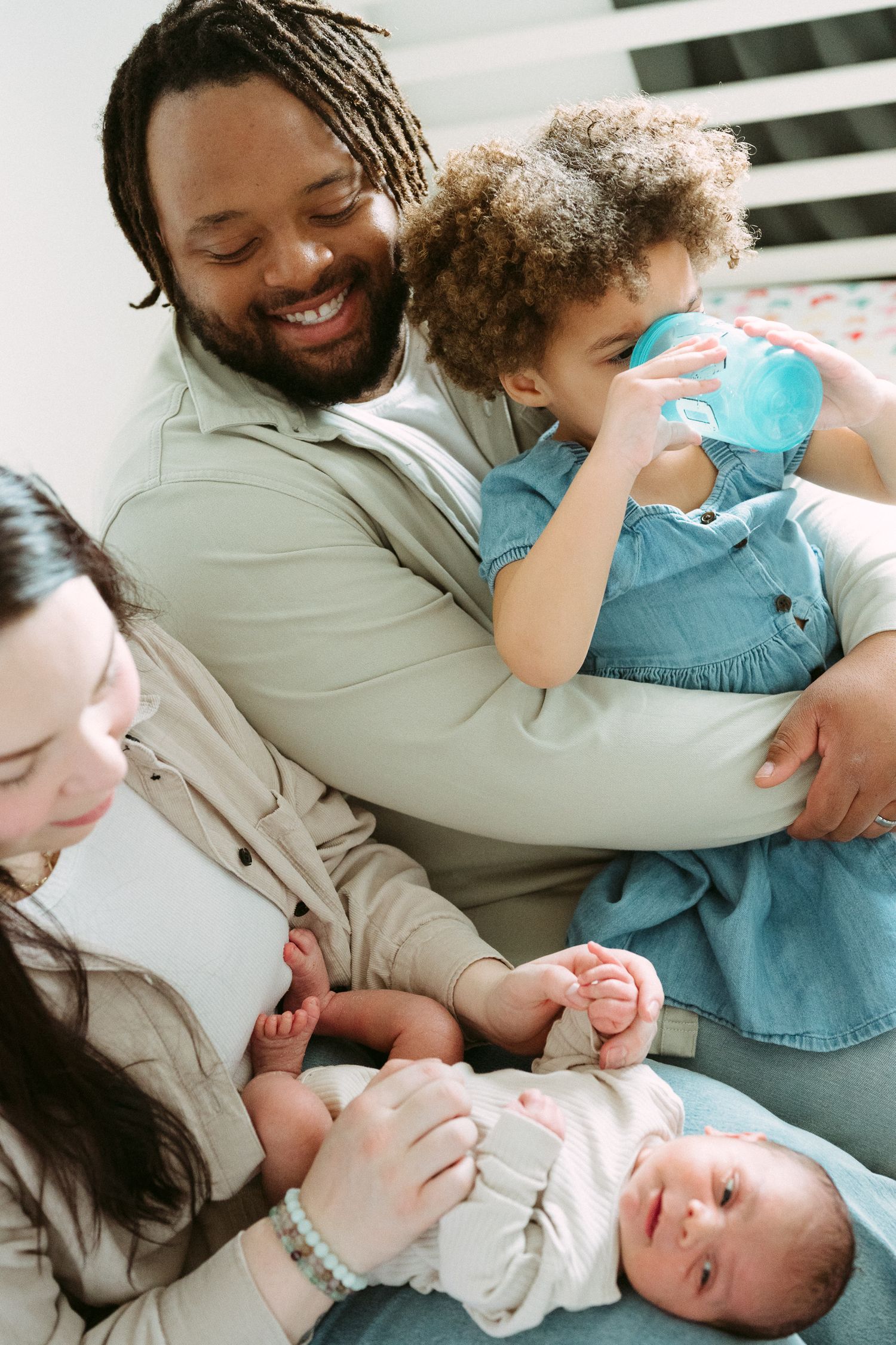 Happy interracial family with smiling father holding toddler girl and mother cradling newborn baby together.