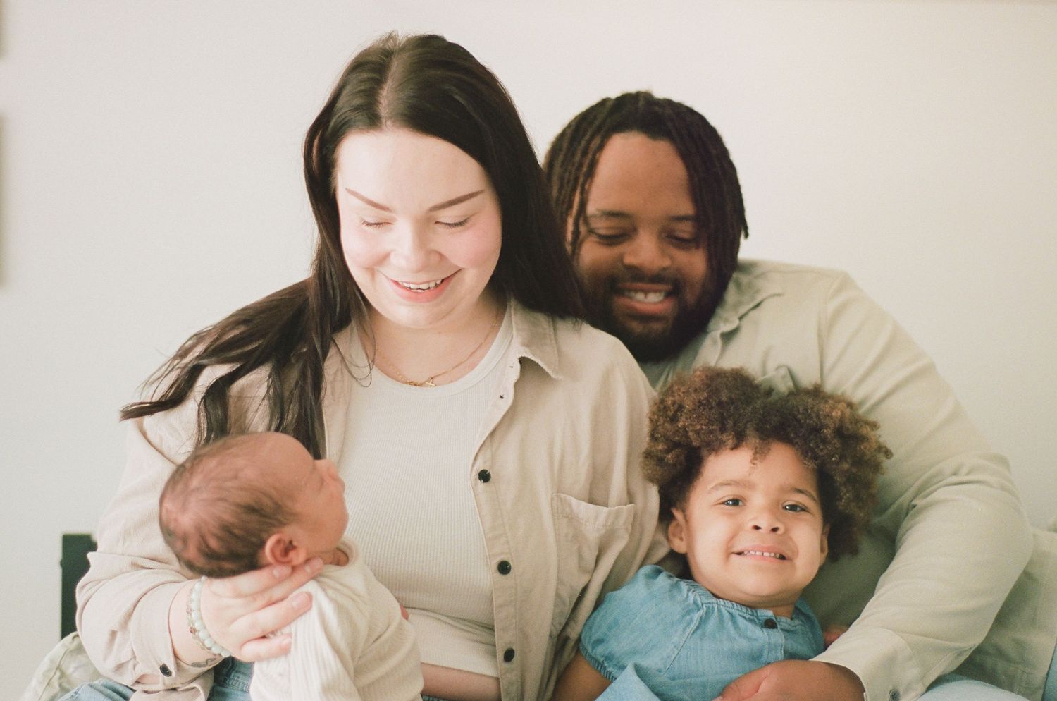 Smiling interracial family with newborn baby and toddler posing together for a portrait photo.
