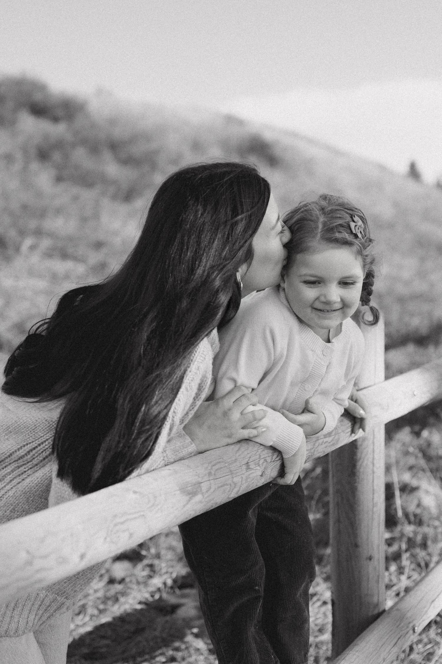 Black and white candid moment of parent and child sharing a tender moment by a wooden fence.