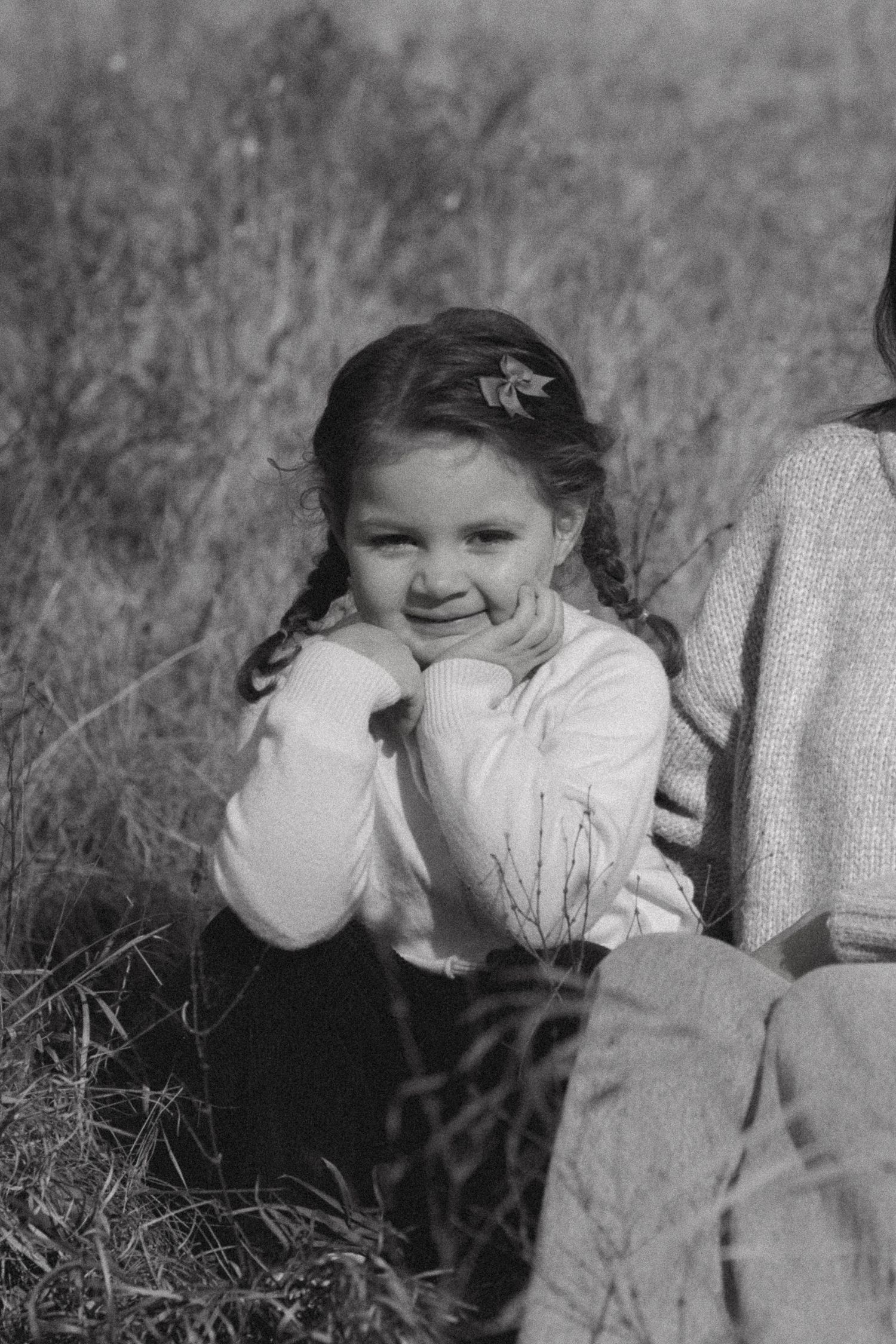 Black and white photo showing a child blowing bubbles in a grassy field on a sunny day.