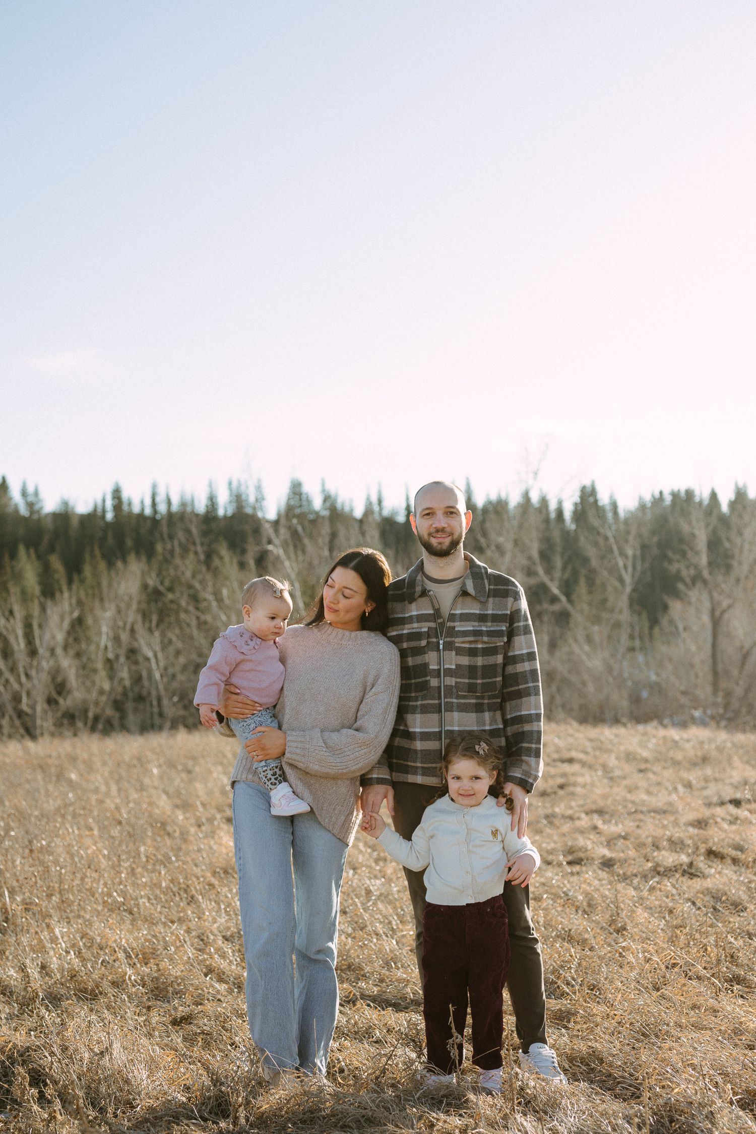 A family stands together in a field with tall trees in the background during golden hour.