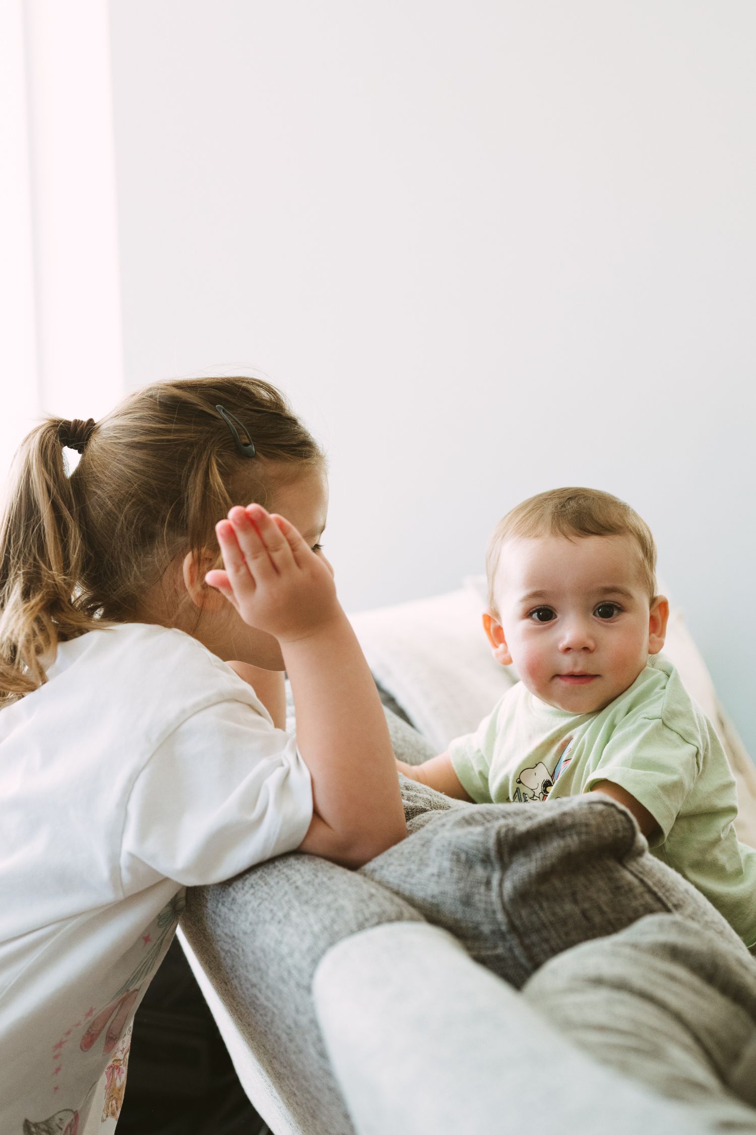 Tender bonding moment between siblings on a light colored background.