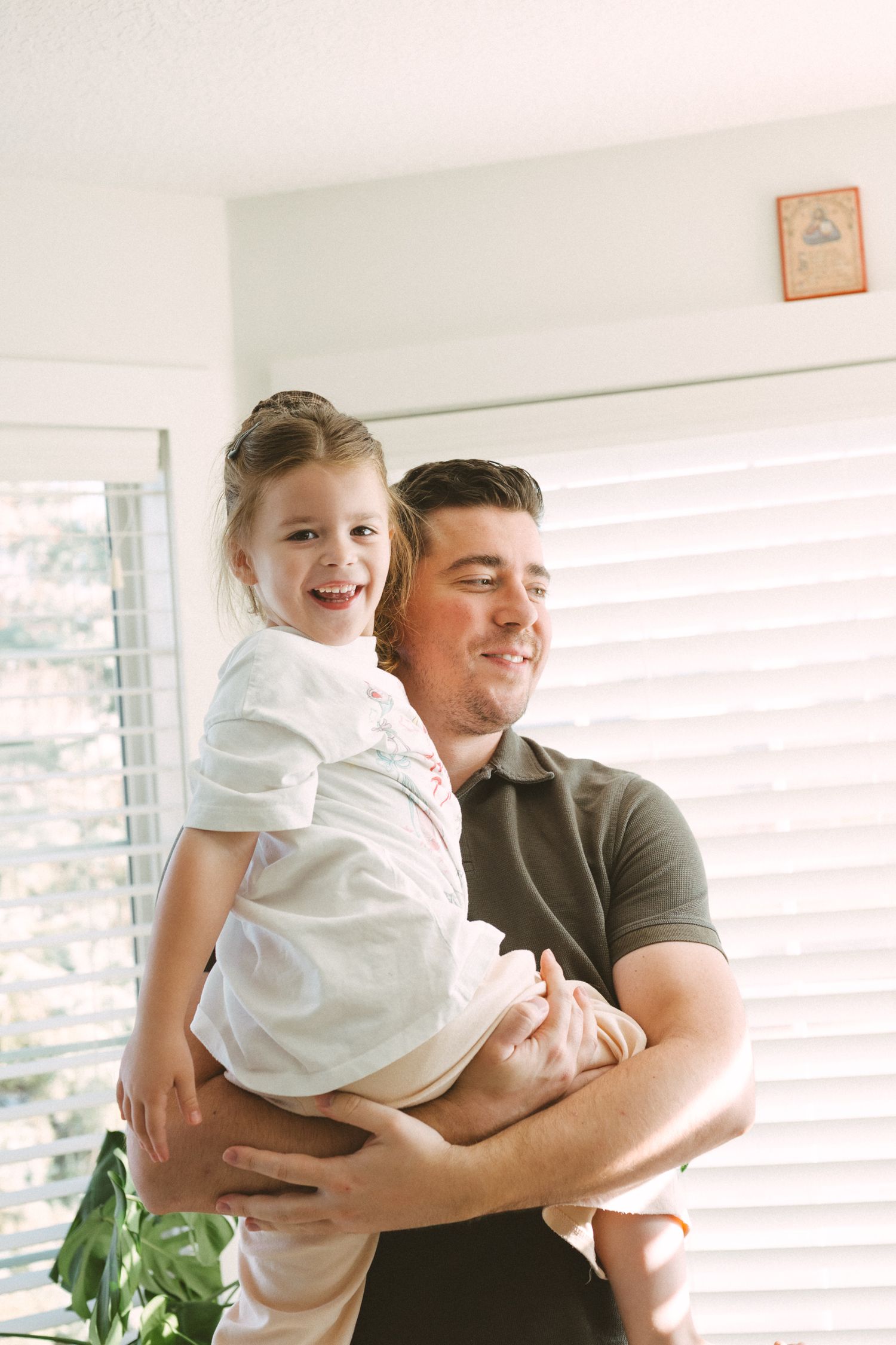 Parent and child sharing joyful moments together in a bright sunlit room with white blinds.