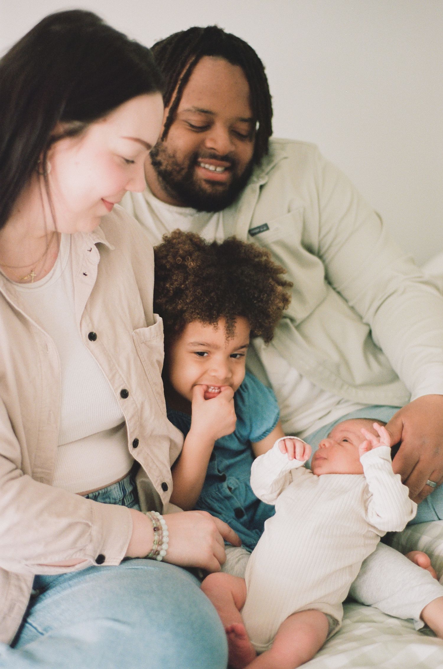 Happy multiracial family with mother, father, toddler, and newborn baby bonding together on bed.