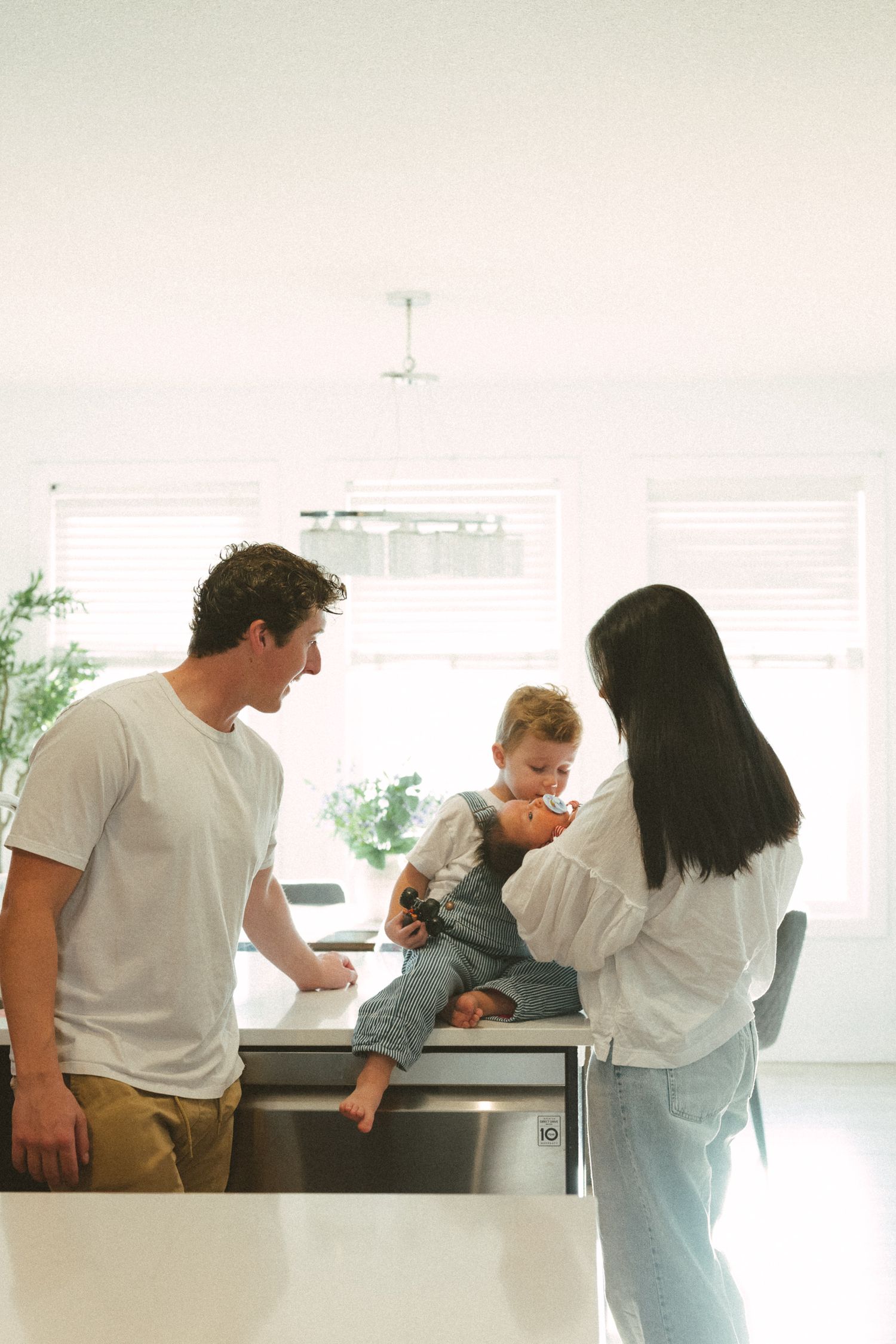 Family spending time together in bright modern kitchen with toddler sitting on counter.