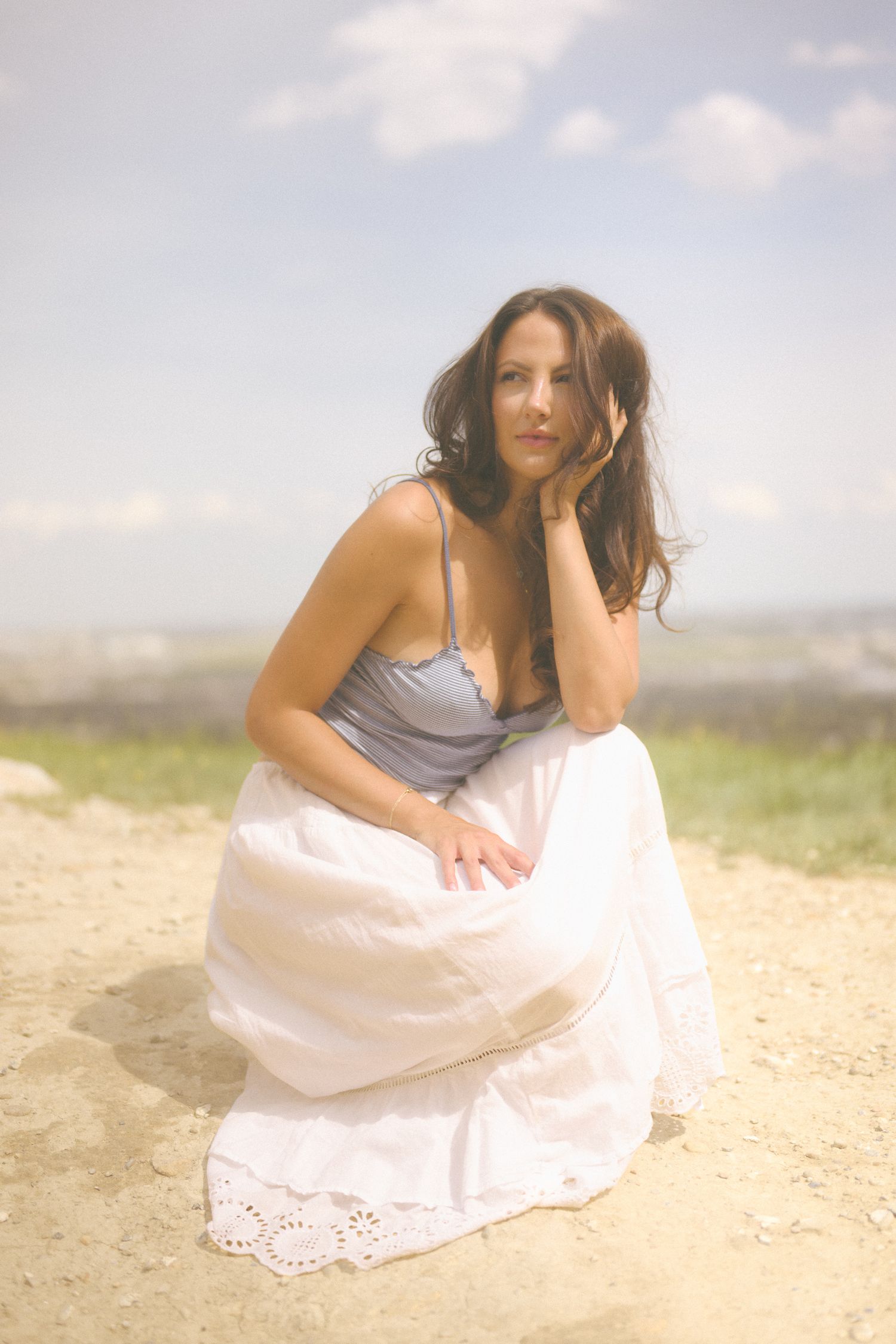 A person in summer attire sits on sandy ground against a bright sky backdrop.