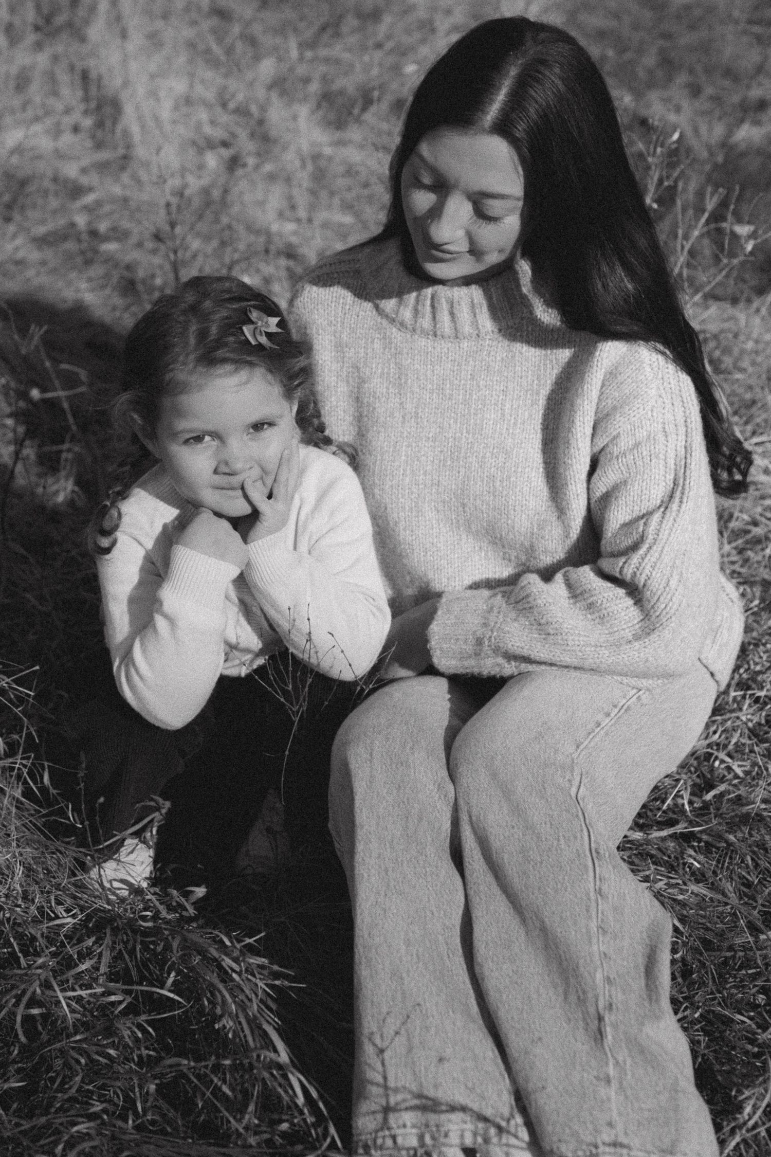 Black and white photo series showing two people in sweaters sitting together in grass with intimate poses.