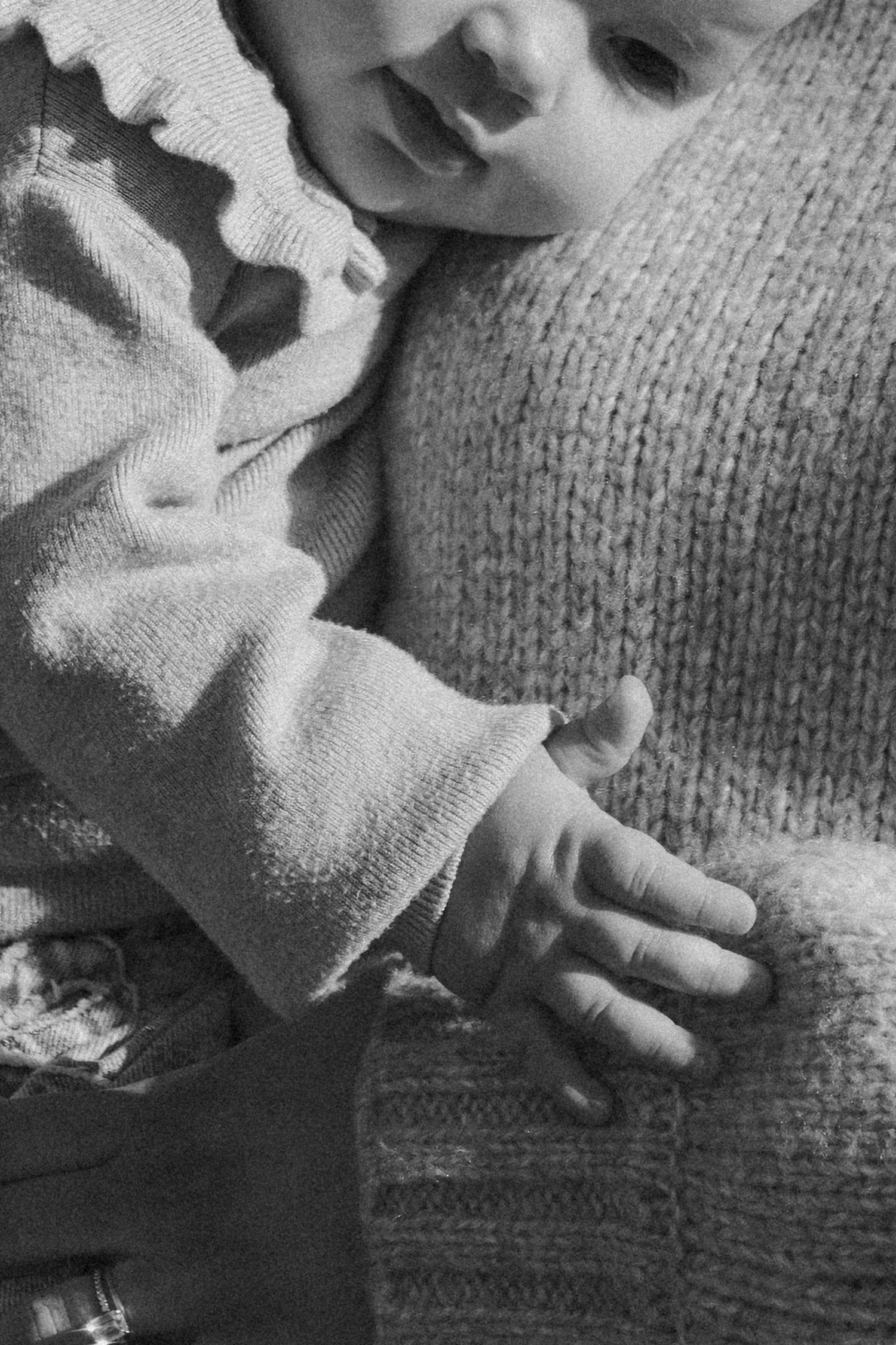 Close-up black and white photo of a baby's tiny hand resting on a knitted sweater texture.