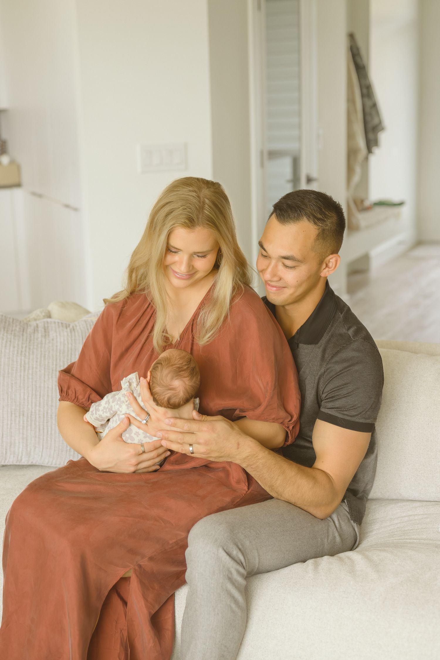 Couple relaxing together on white couch while holding newborn baby.