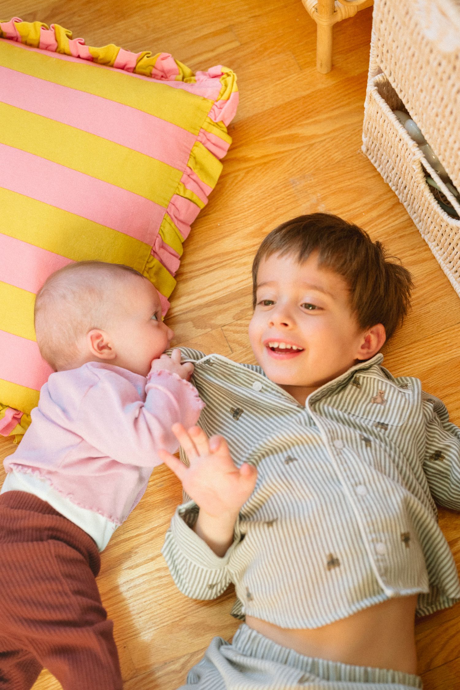 Two children sharing a joyful moment while lying on striped cushion near furniture.