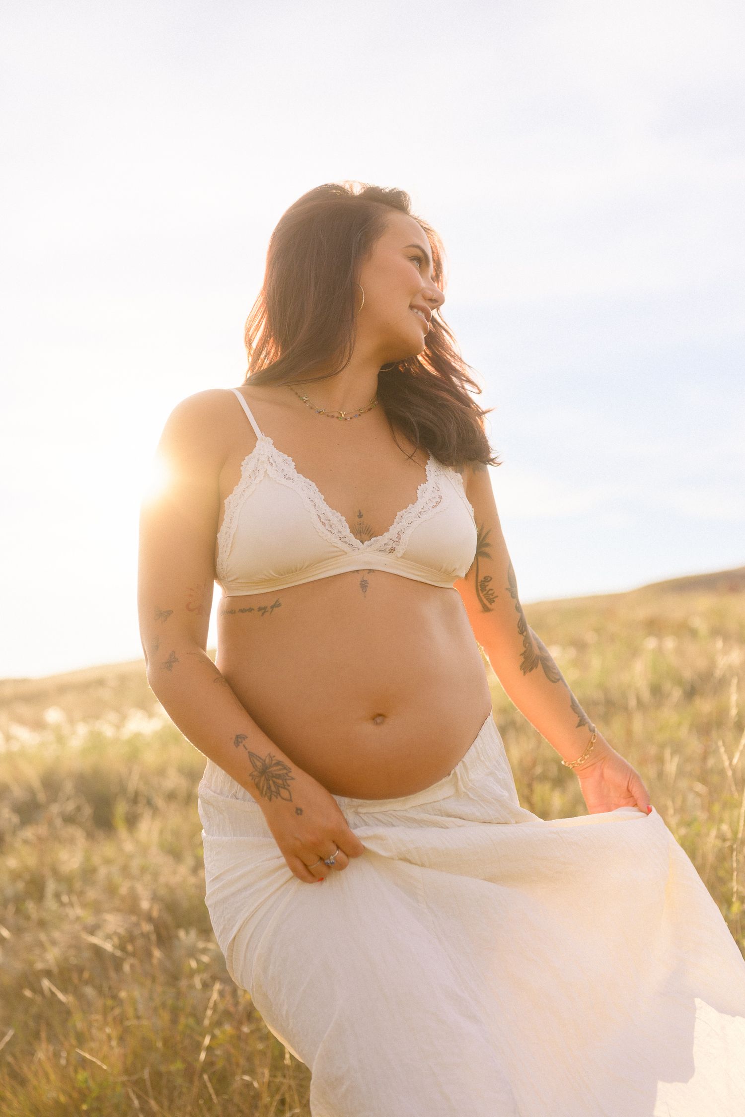 Candid maternity moments photographed in natural light showing white dress and tattoos.