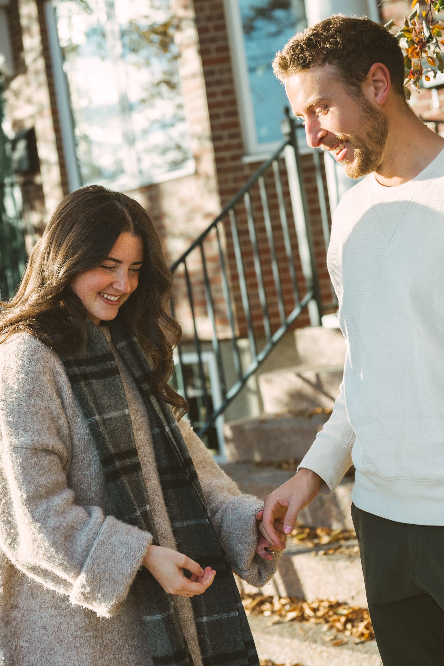 A couple shares a joyful moment together outdoors on a sunny autumn day with fallen leaves in the background.