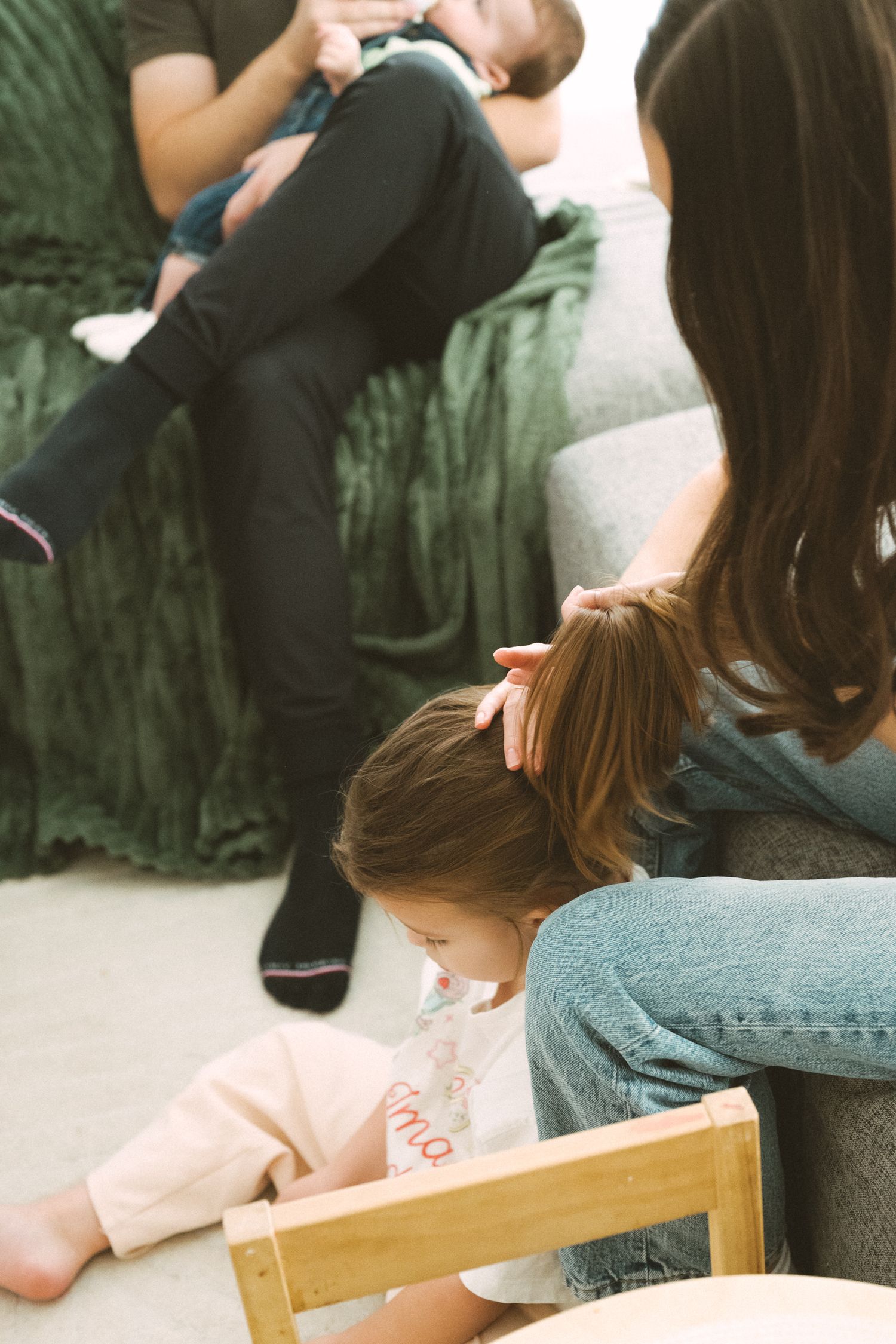 Family relaxing together on a couch with green foliage visible in the background through large windows.