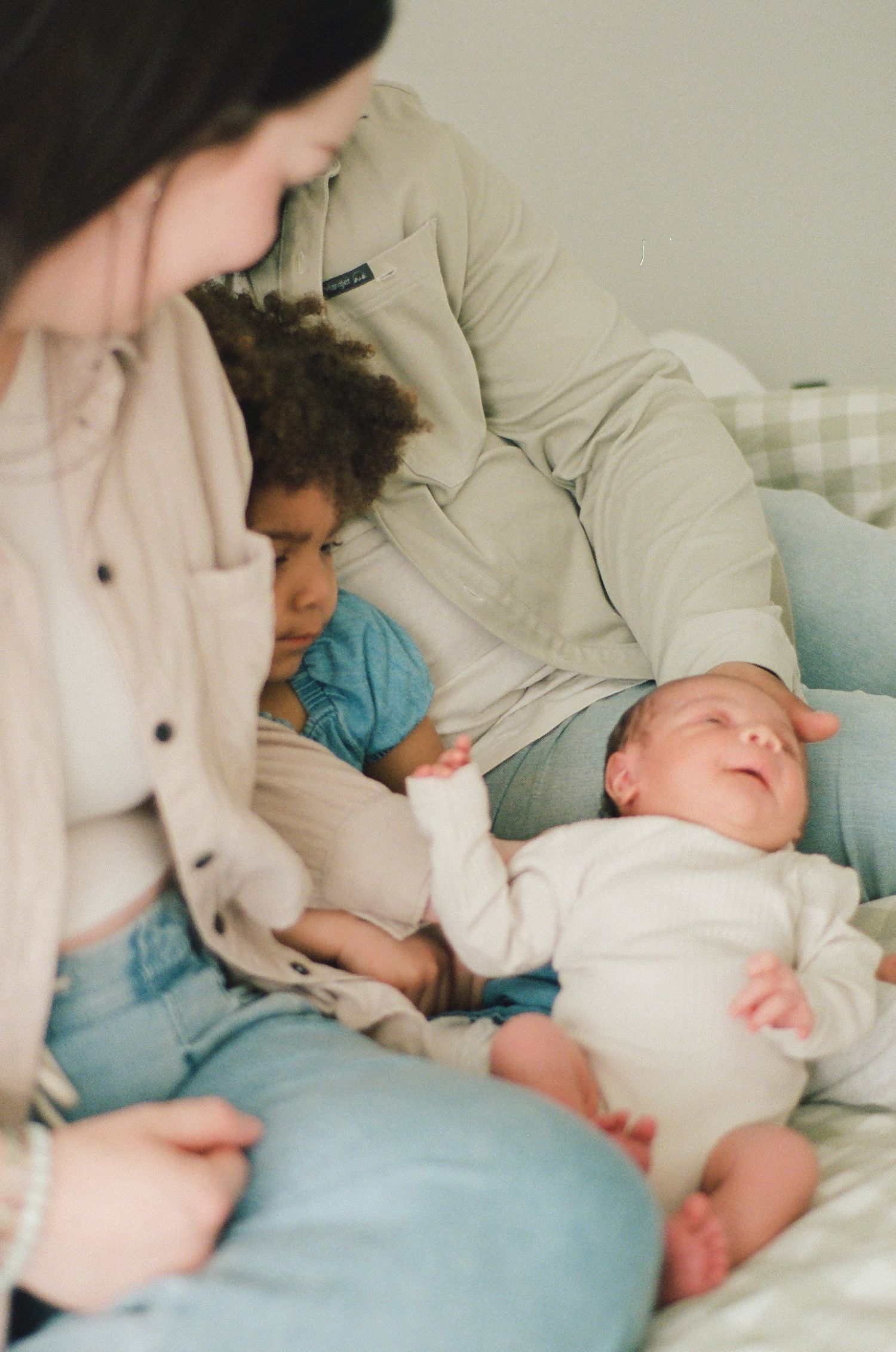 A multiracial family with a toddler and mother admires their peaceful newborn baby on a bed.