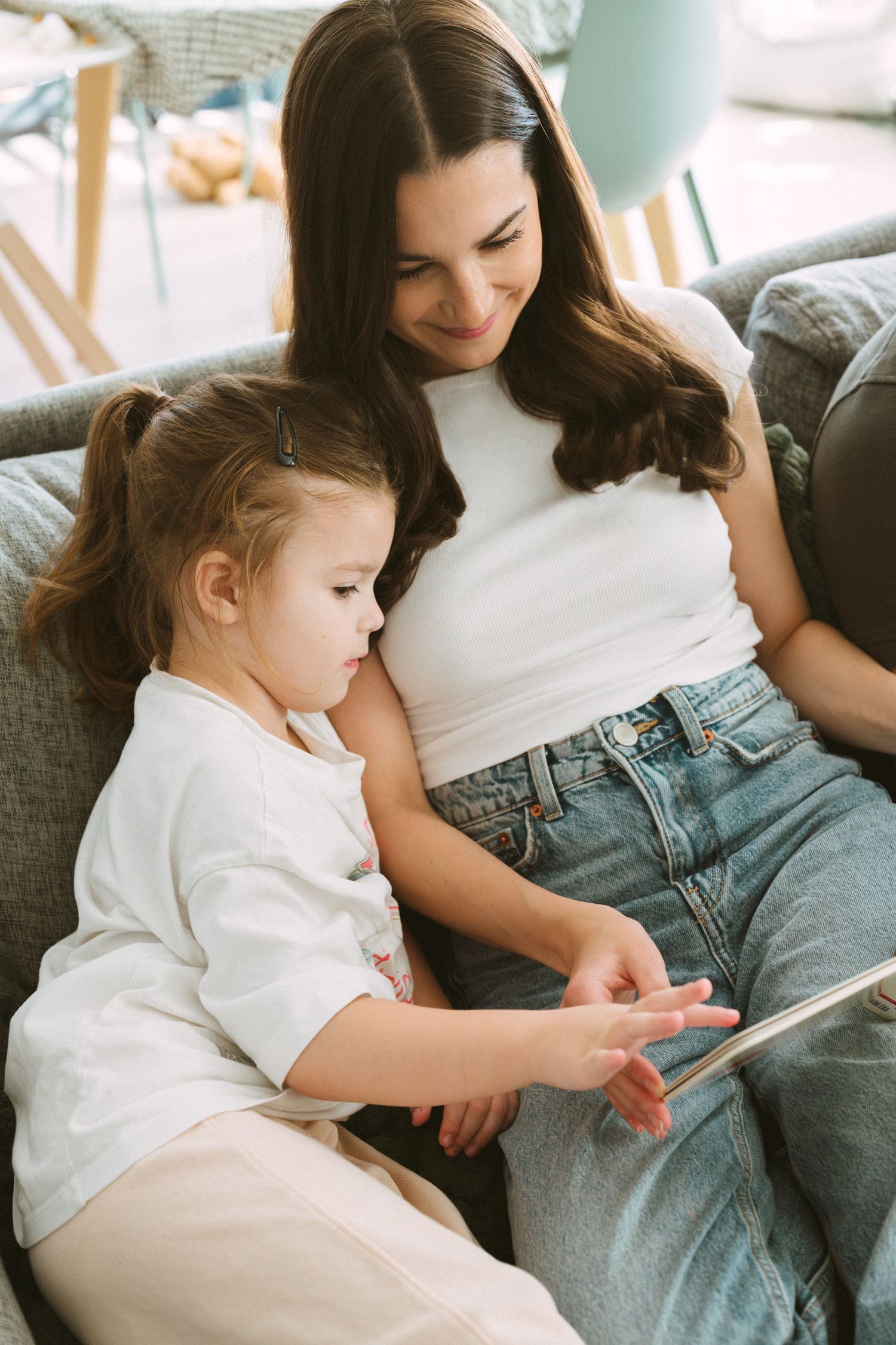 Parent and child sit together on gray couch reading a book in a series of intimate bonding moments.