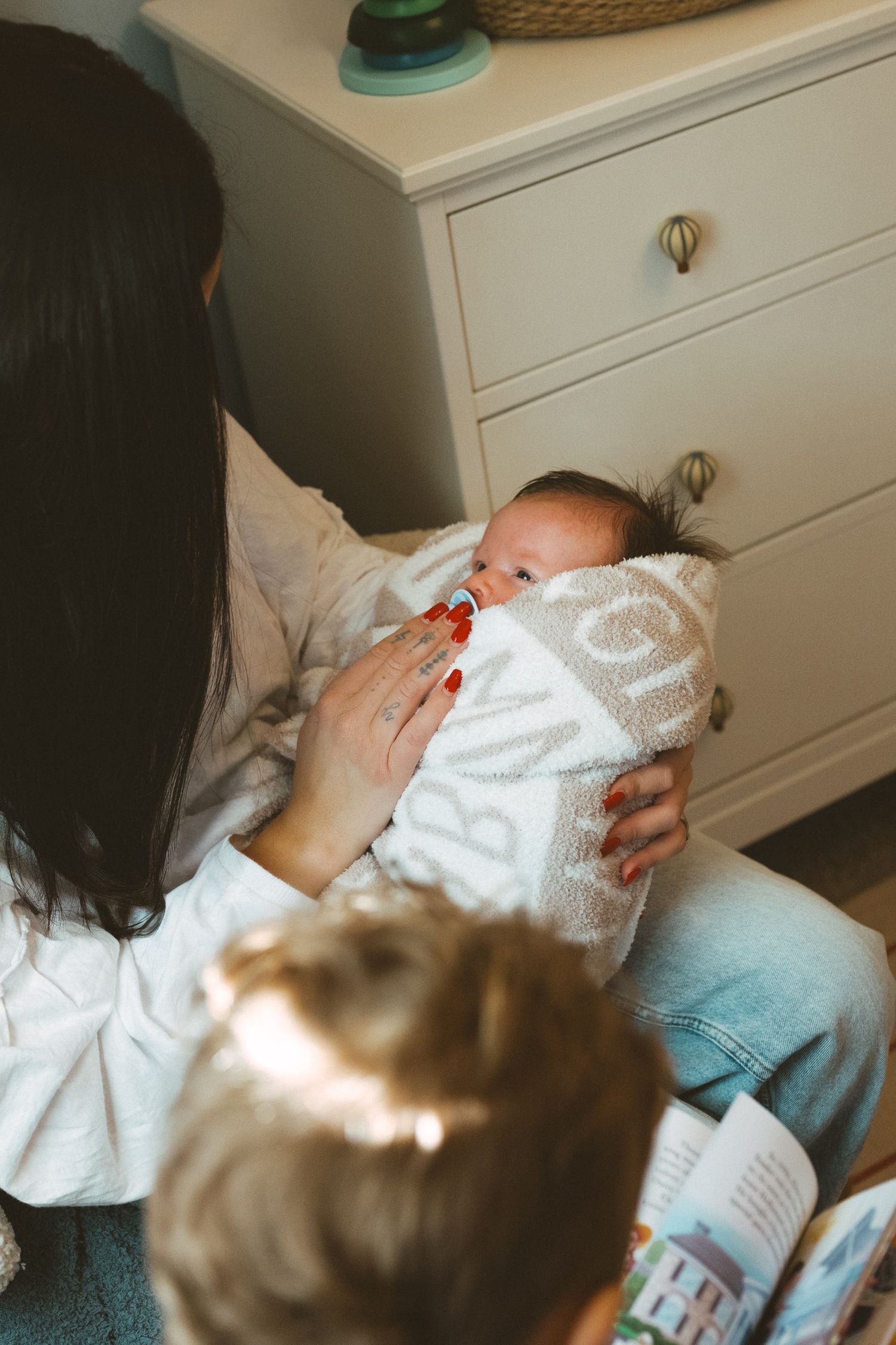 A tender moment showing a baby being held and cradled in a white blanket against a light background.