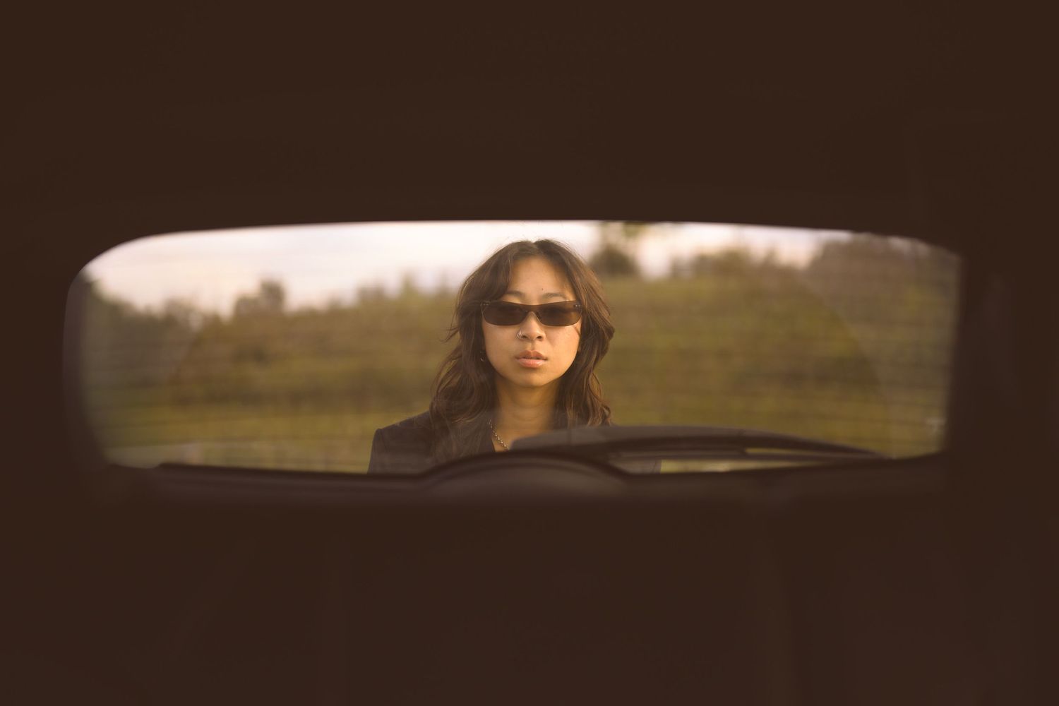 Cinematic view through a car window showing a rural landscape at sunset.