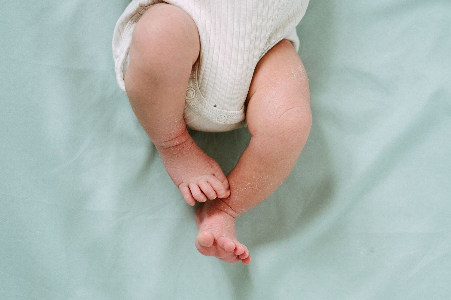 Close-up of newborn baby tiny feet and legs on a soft mint green blanket.