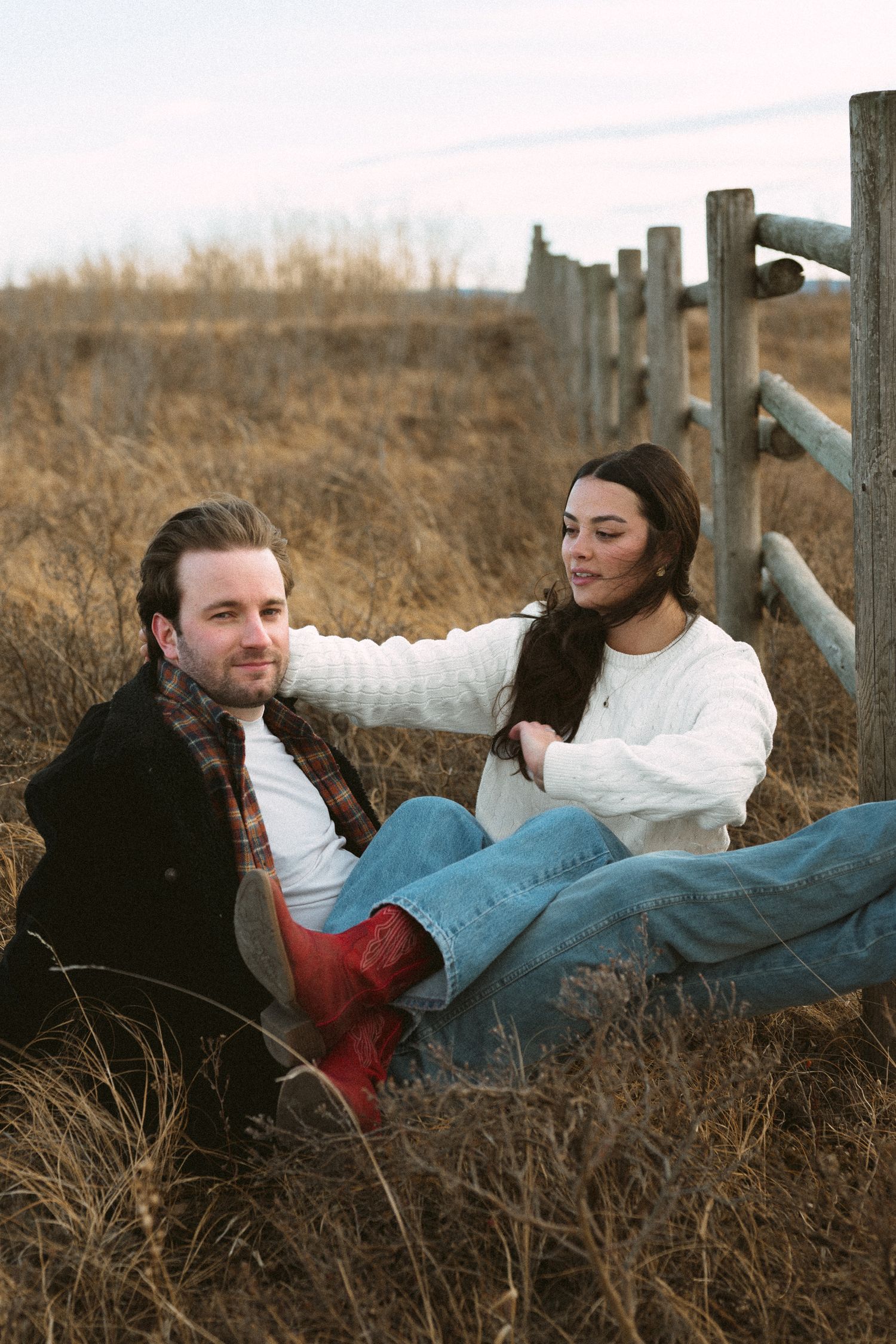 Two people relax together against a wooden fence in a golden field during autumn.