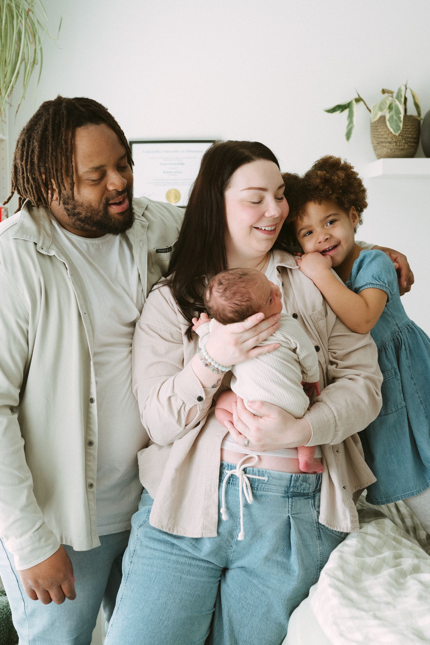 Happy interracial family with newborn baby and young daughter smiling together in a bright home setting.