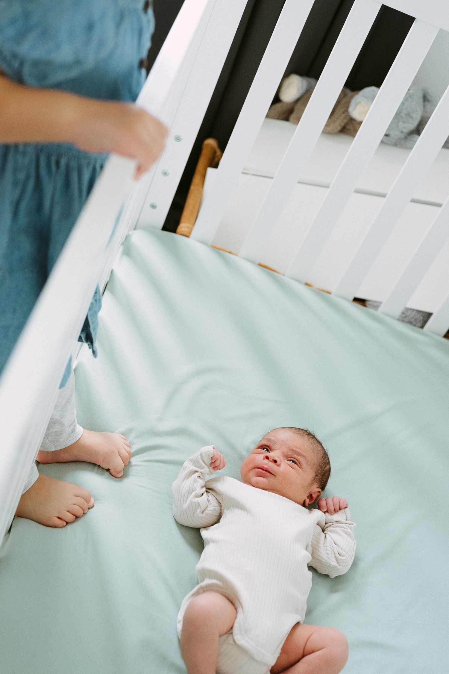Newborn baby lying in a white crib on a light blue sheet.
