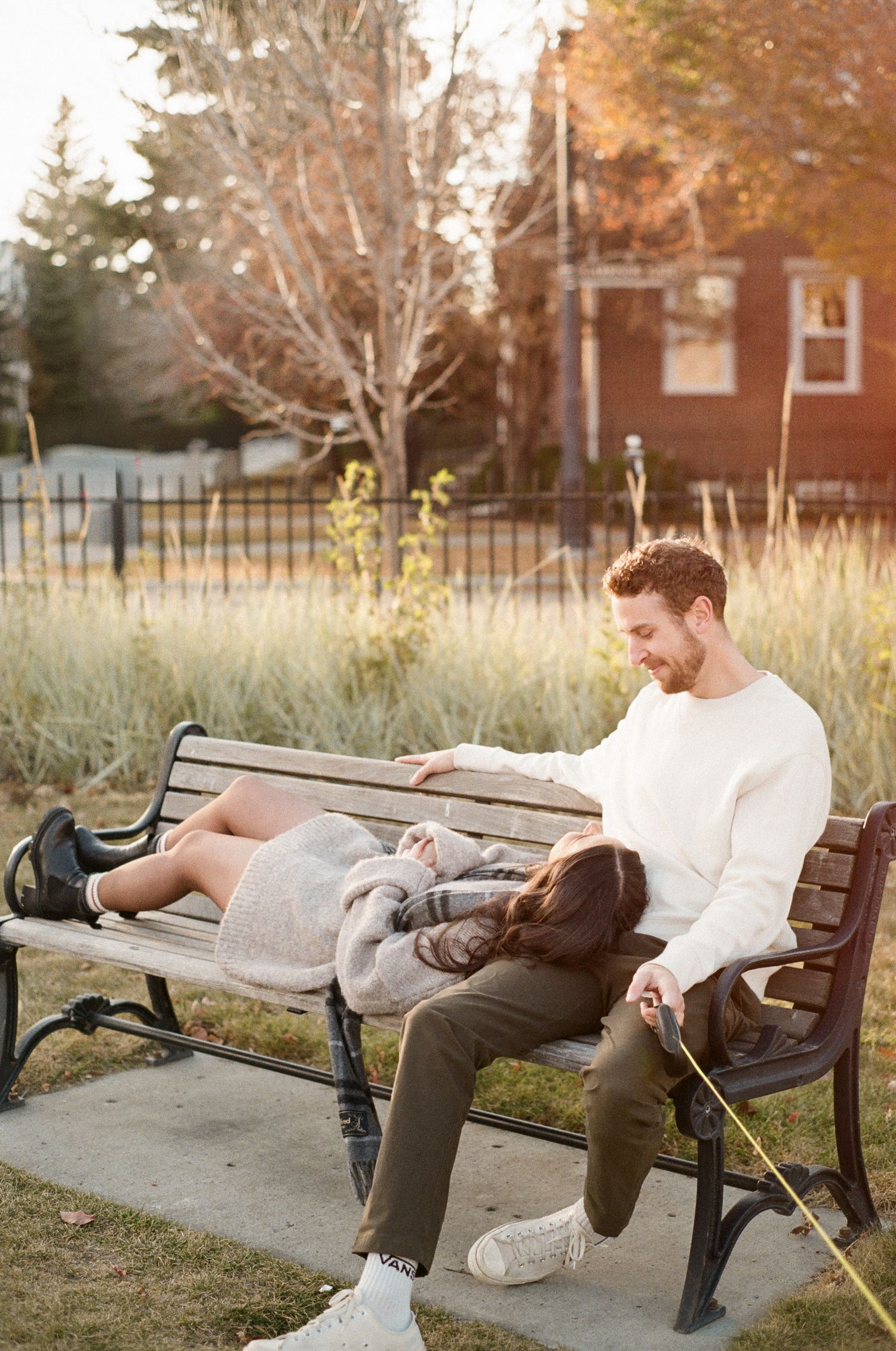 Couple relaxing together on park bench during golden hour with autumn foliage in background.