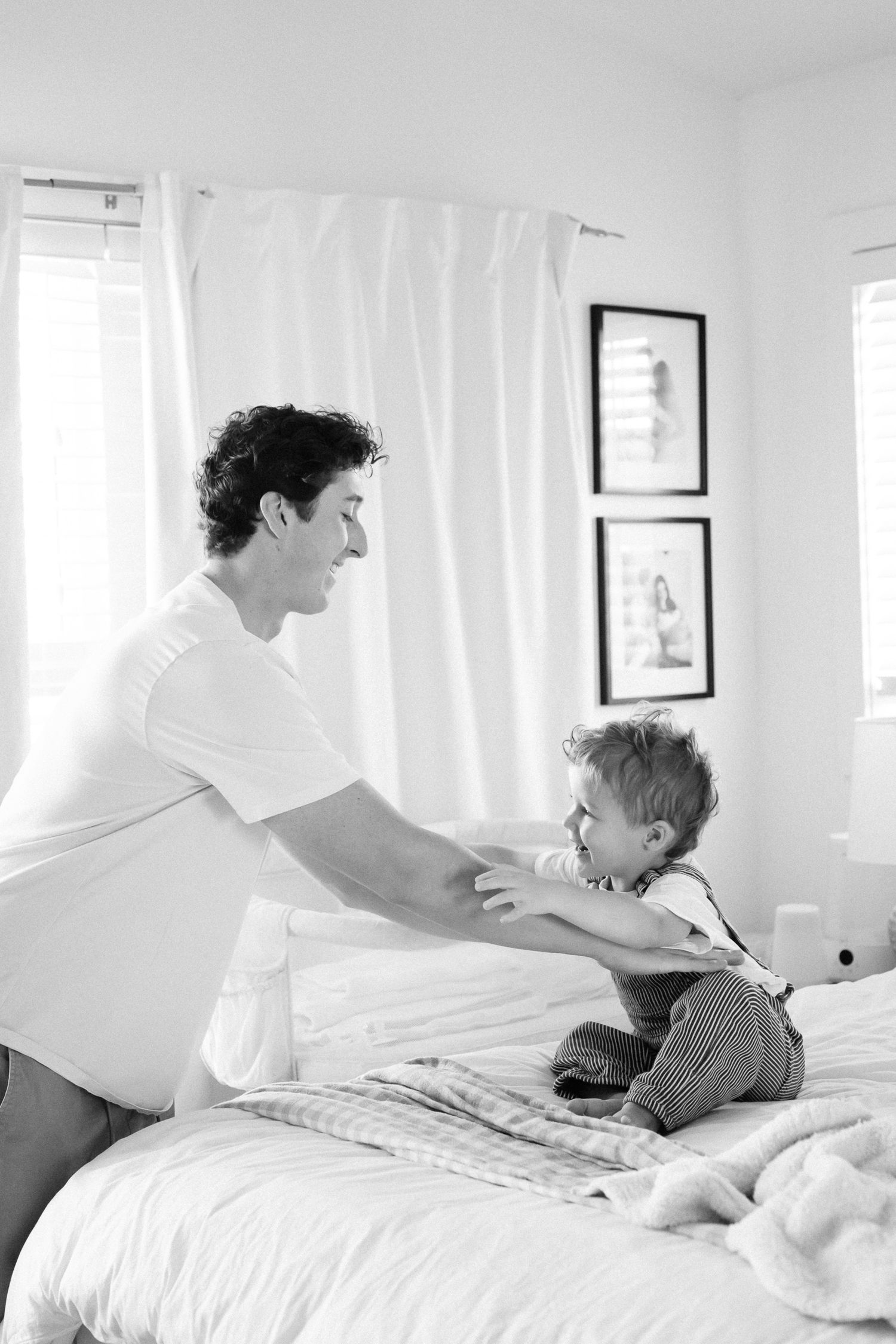 Black and white series showing intimate bedtime moments in a bright white bedroom.