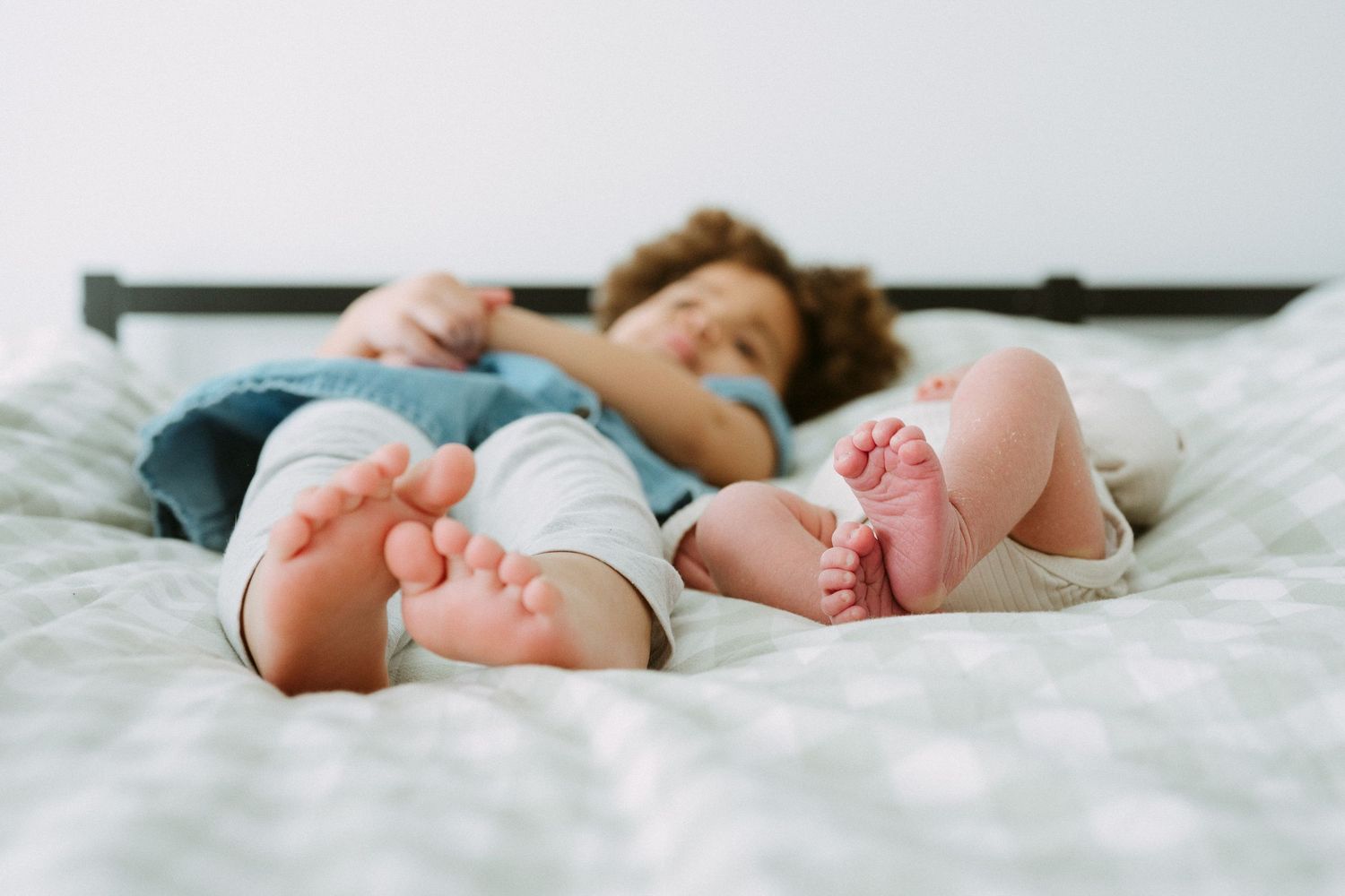 Two young children lying on a bed with bare feet in the foreground, captured in a cozy and peaceful moment.