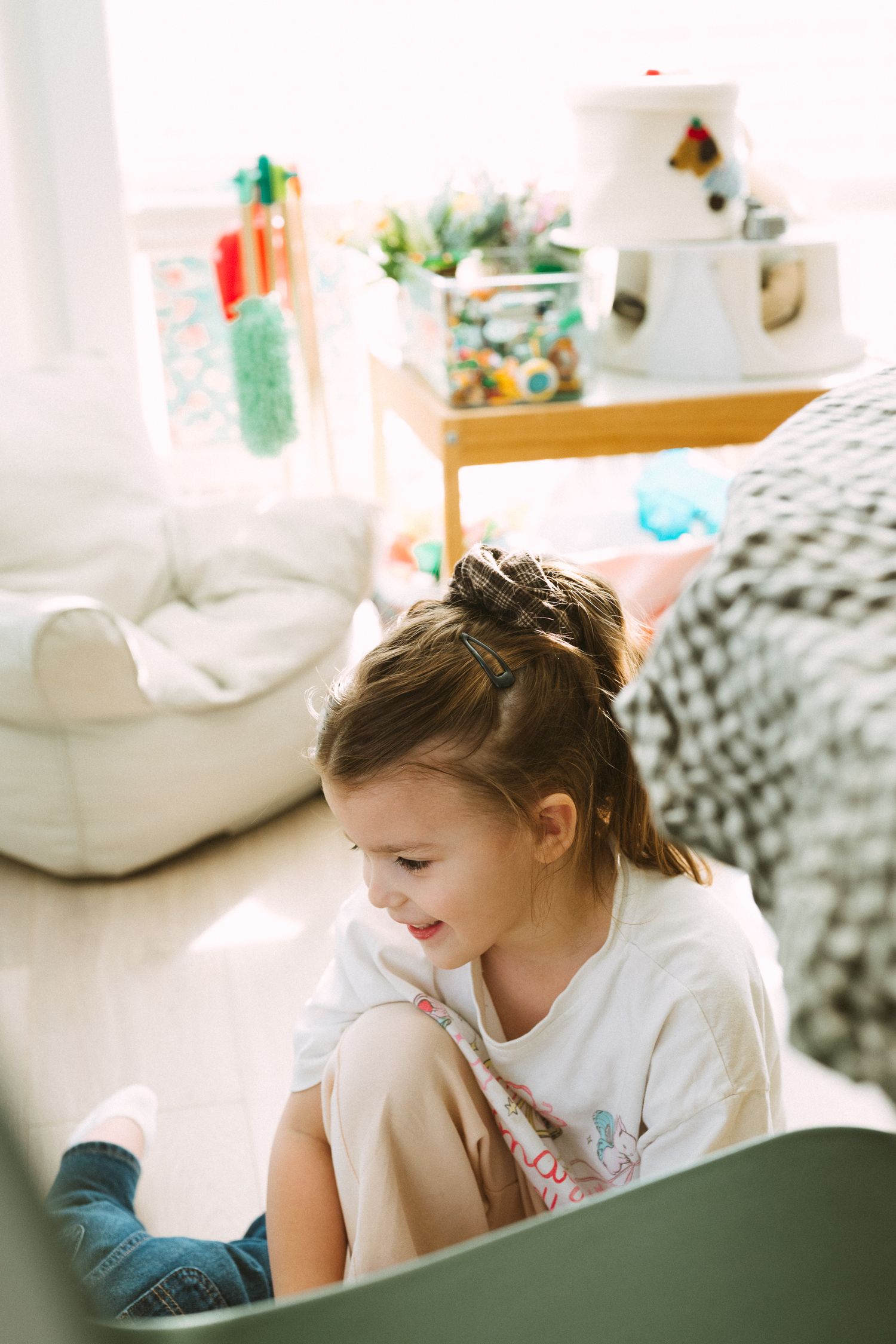 Child in white shirt sits comfortably in a cozy bedroom setting with decorative elements in the background.