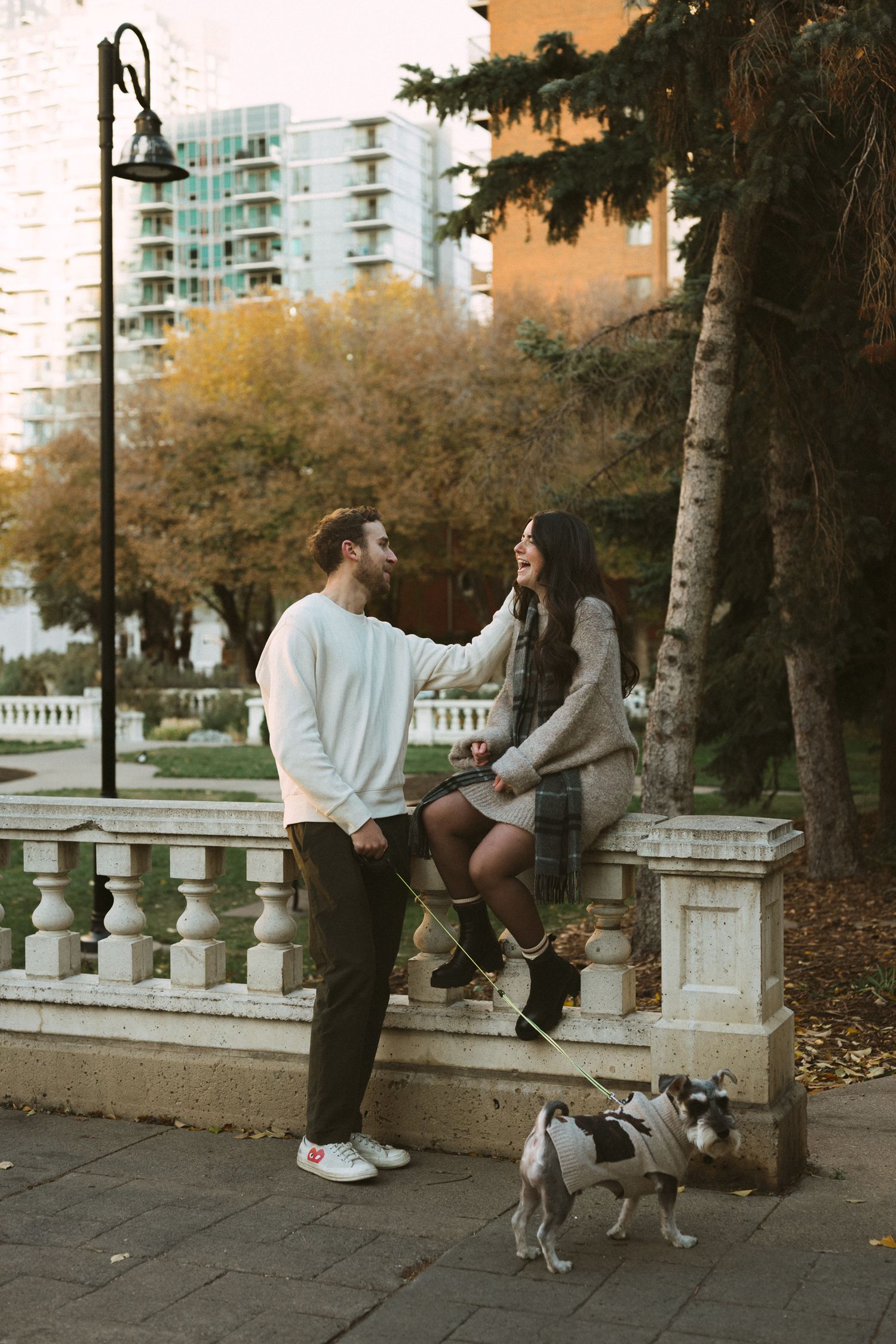 A couple shares a romantic moment on stone steps while their dog sits nearby during an autumn evening in the city.