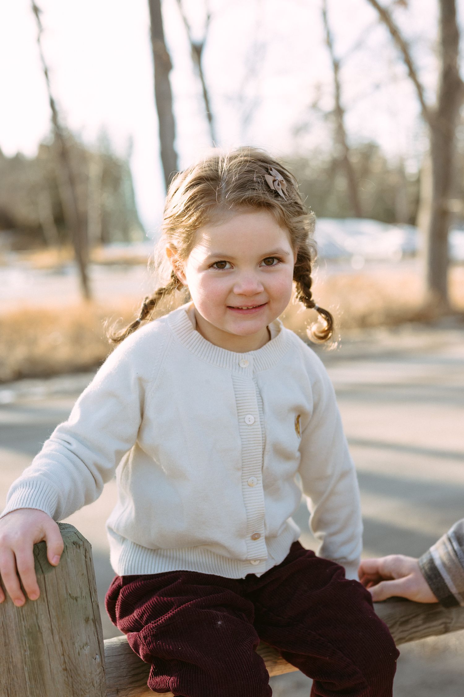 A series of candid shots showing a child in a white sweater sitting on a wooden fence on a sunny day.