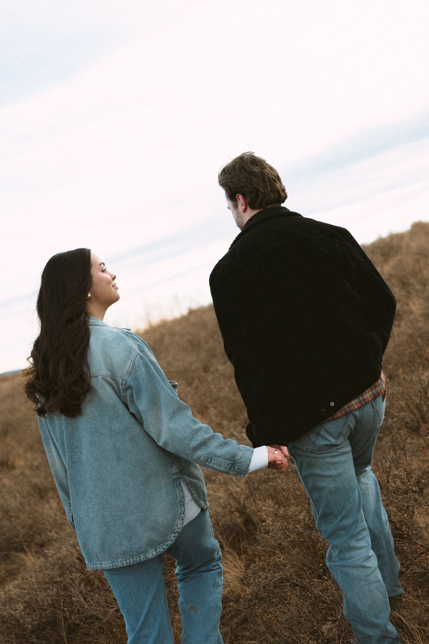 A playful scene shows two people in matching denim outfits walking on a hillside.
