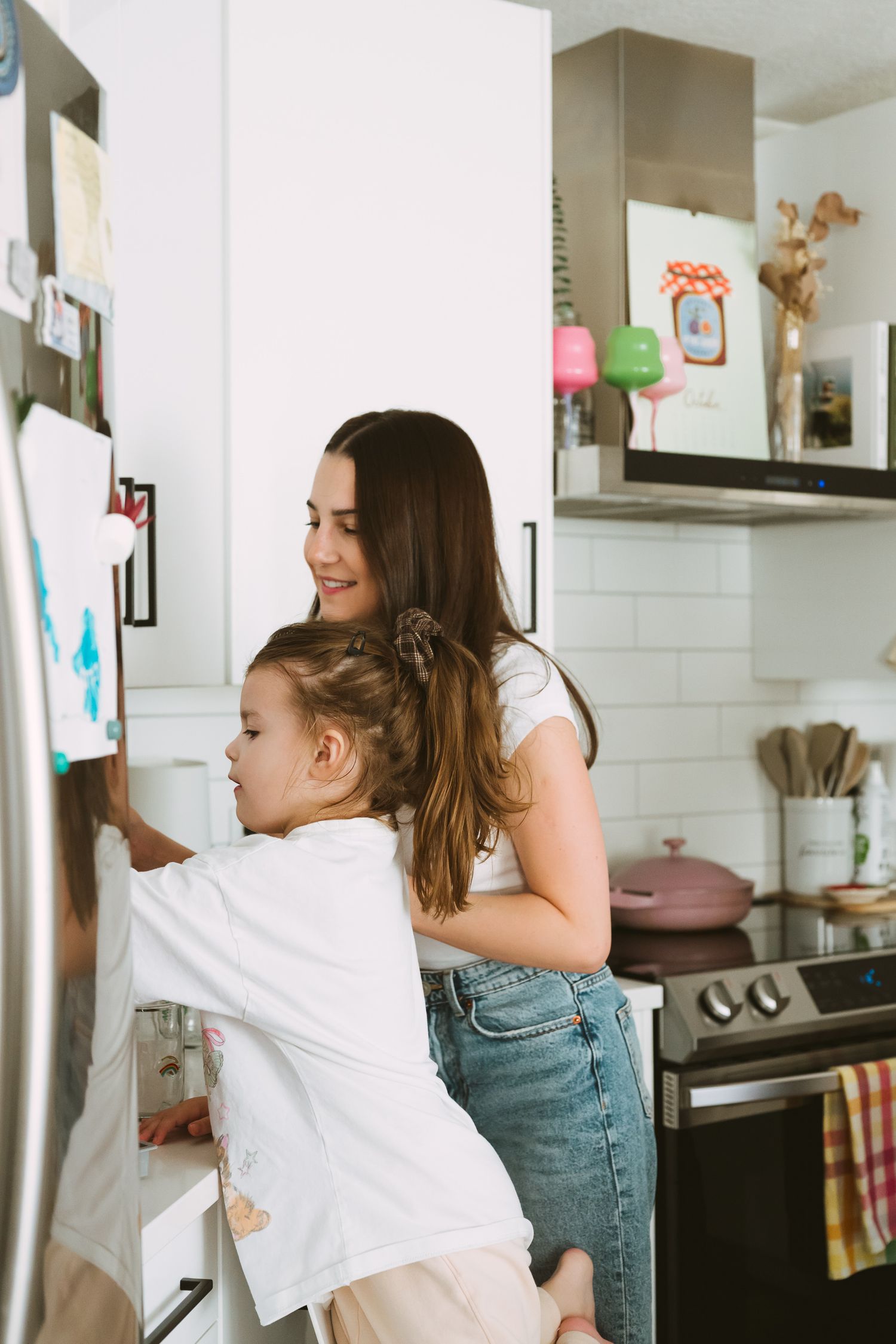 Parent and child looking at items posted on refrigerator in modern white kitchen.