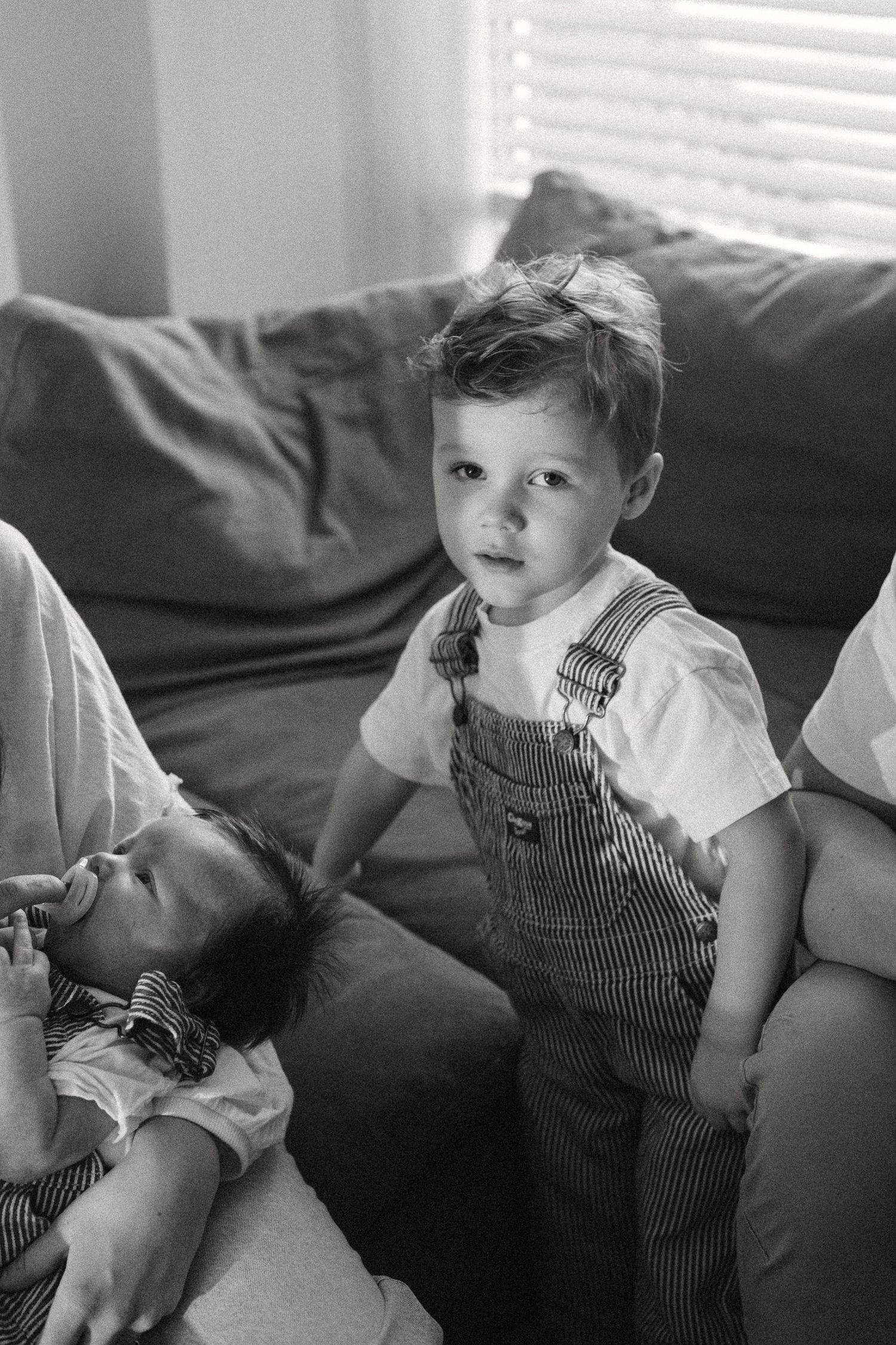 A small child in striped overalls sits on a couch in a black and white photo.