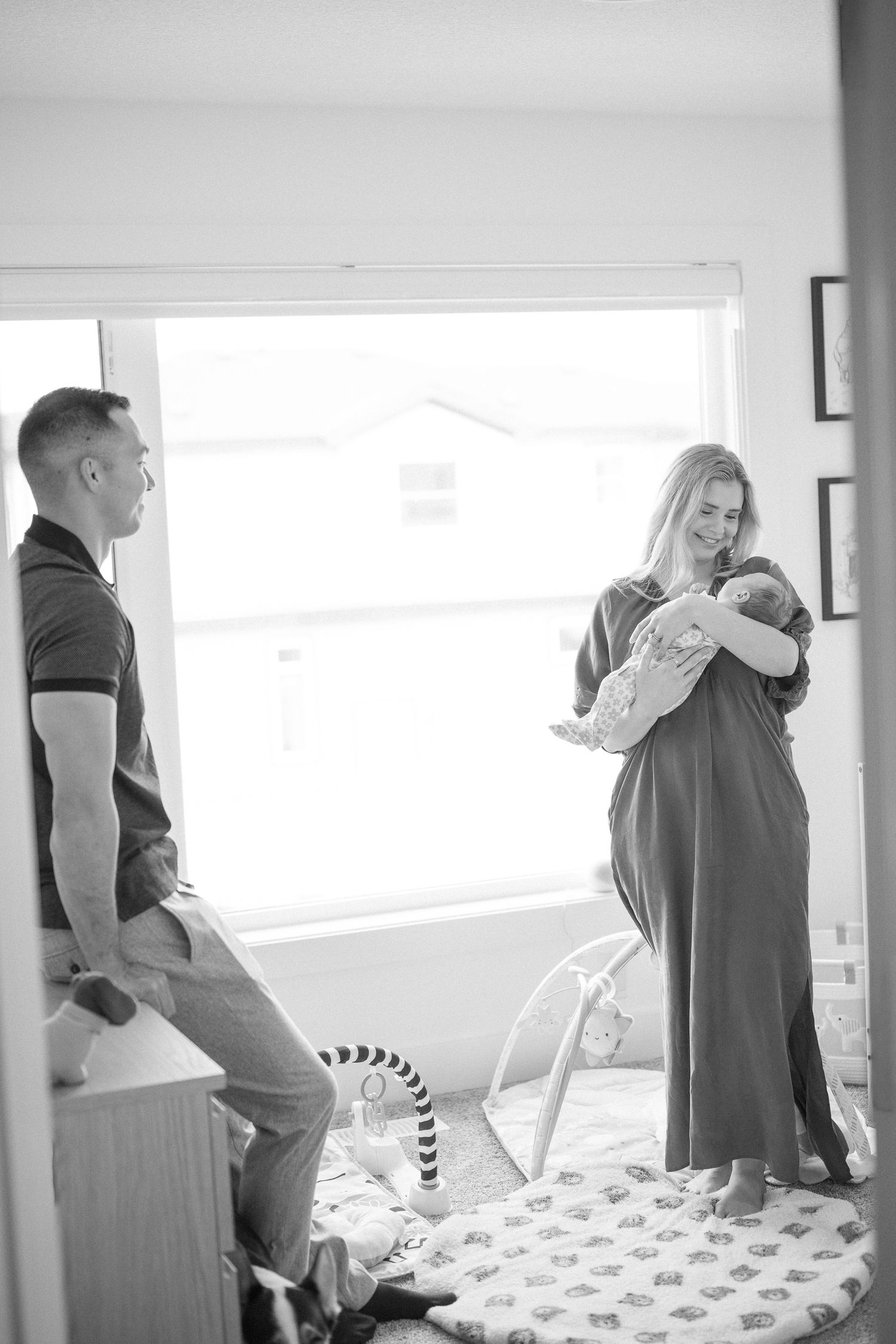 Parents sharing an intimate moment while standing near a bright window.