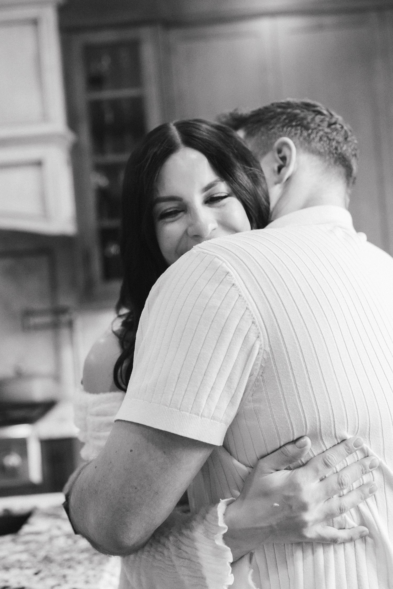 Happy couple sharing a warm embrace in a kitchen, captured in black and white.