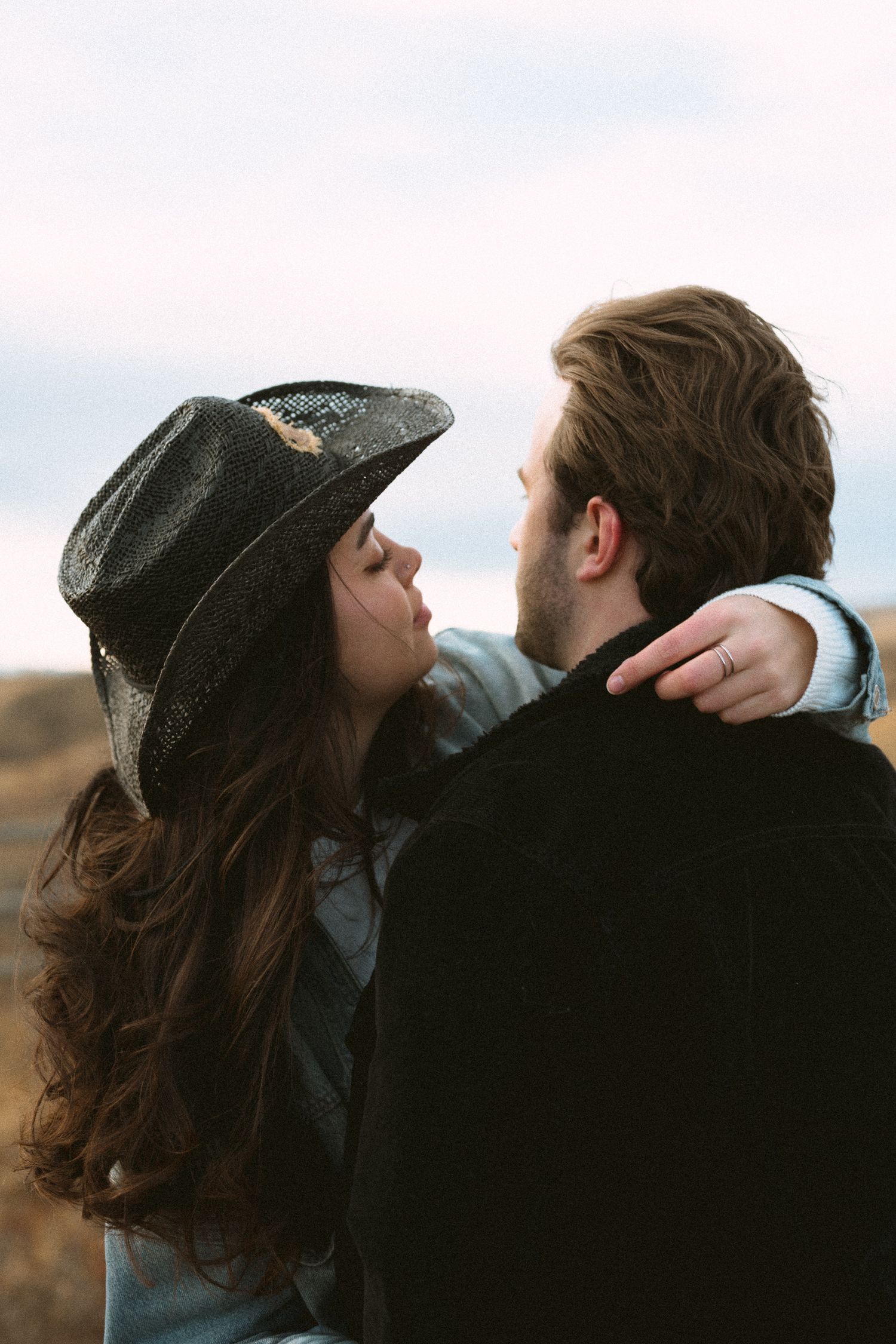 A couple shares an intimate kiss while leaning against a wooden railing at sunset.