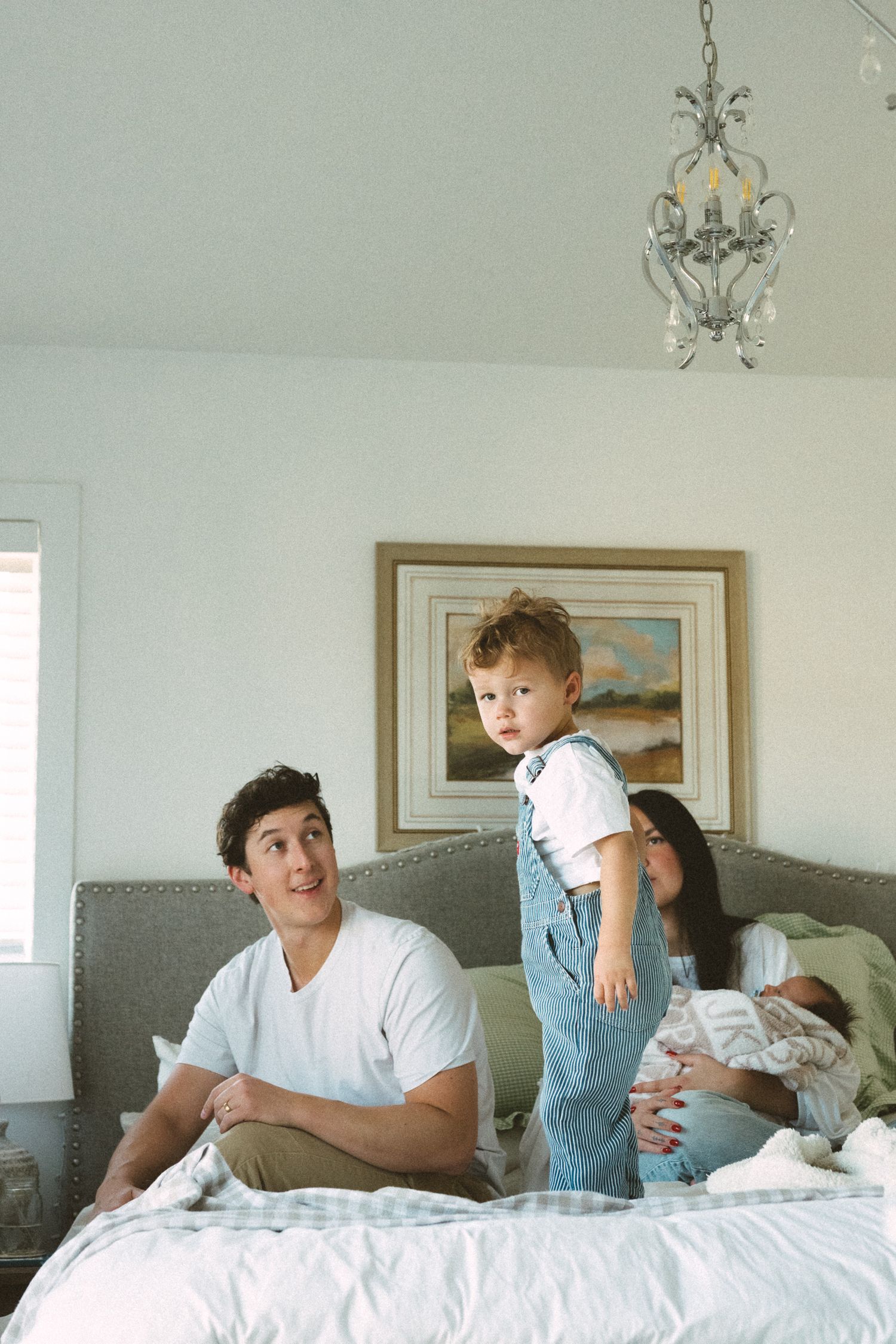 A series of candid moments captured in a bright bedroom with white bedding and framed artwork on the wall.