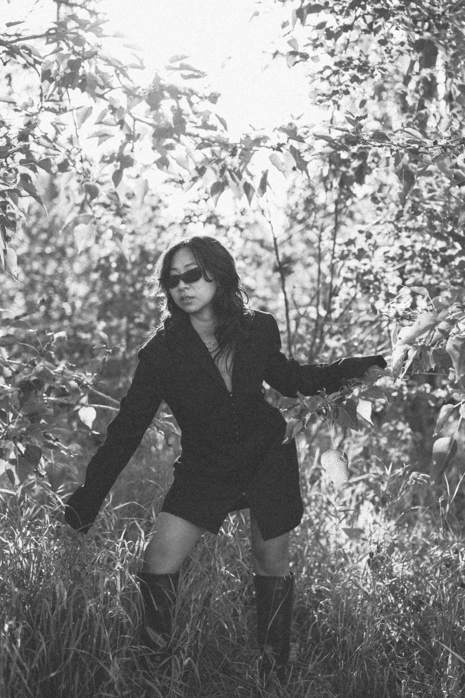 Black and white fashion photo of person in blazer dress posing among leaves.