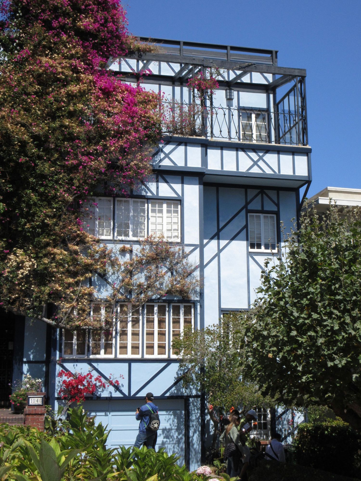 Blue and white three-story house with flowering bougainvillea and architectural details in an urban setting.