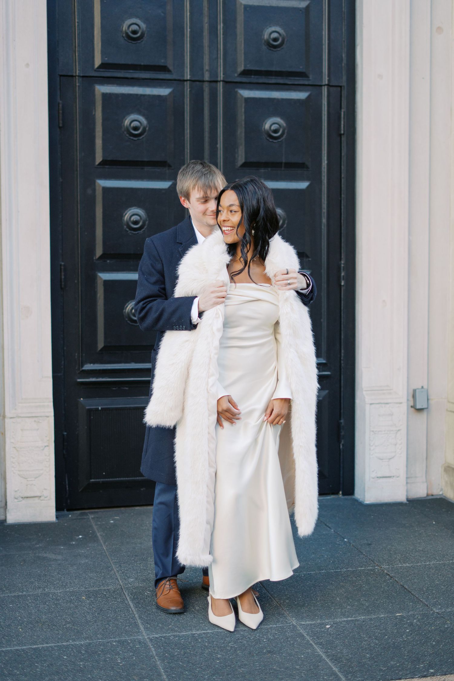 A couple shares an intimate moment against black doors of a historic building.