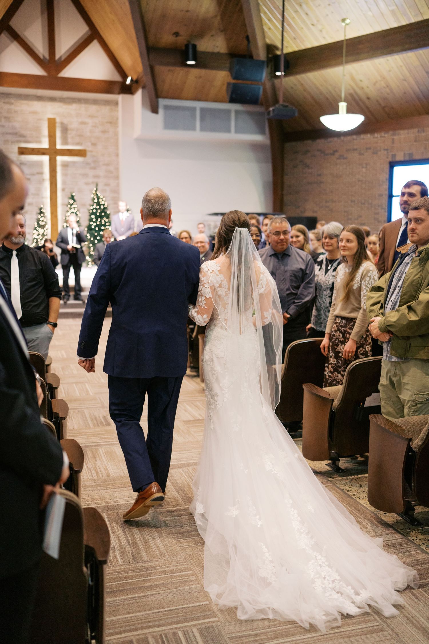 Wedding ceremony procession in a modern church with brick walls and wooden beams.