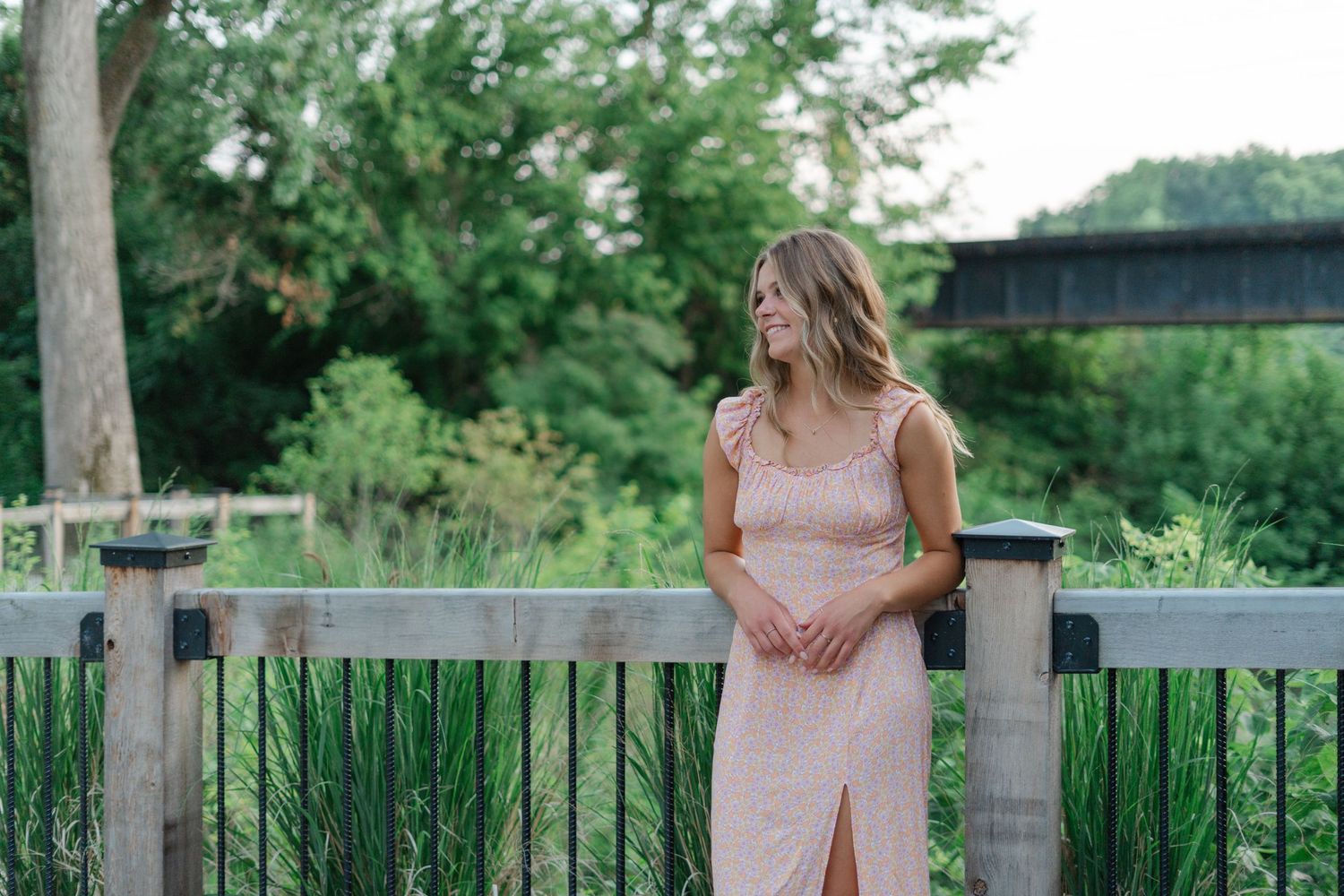 Casual portrait against a wooden railing with green foliage in background.