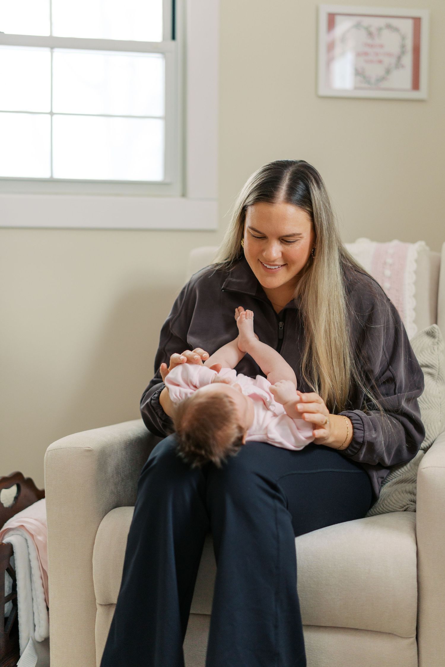 A tender moment with a newborn baby wearing pink being cradled on a beige couch.