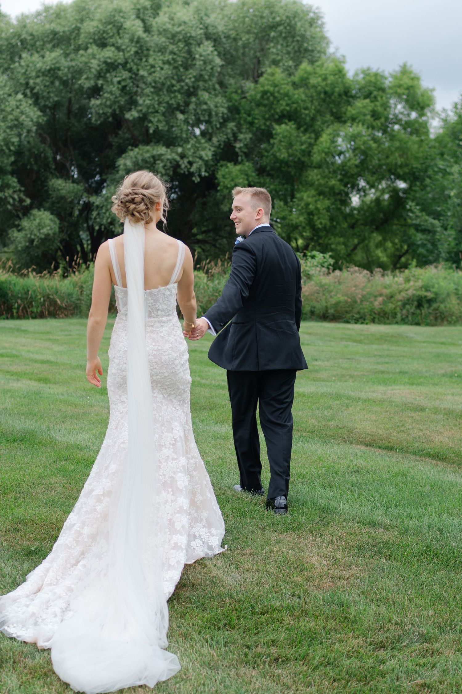 Wedding couple walks together across a lush green field on their special day.