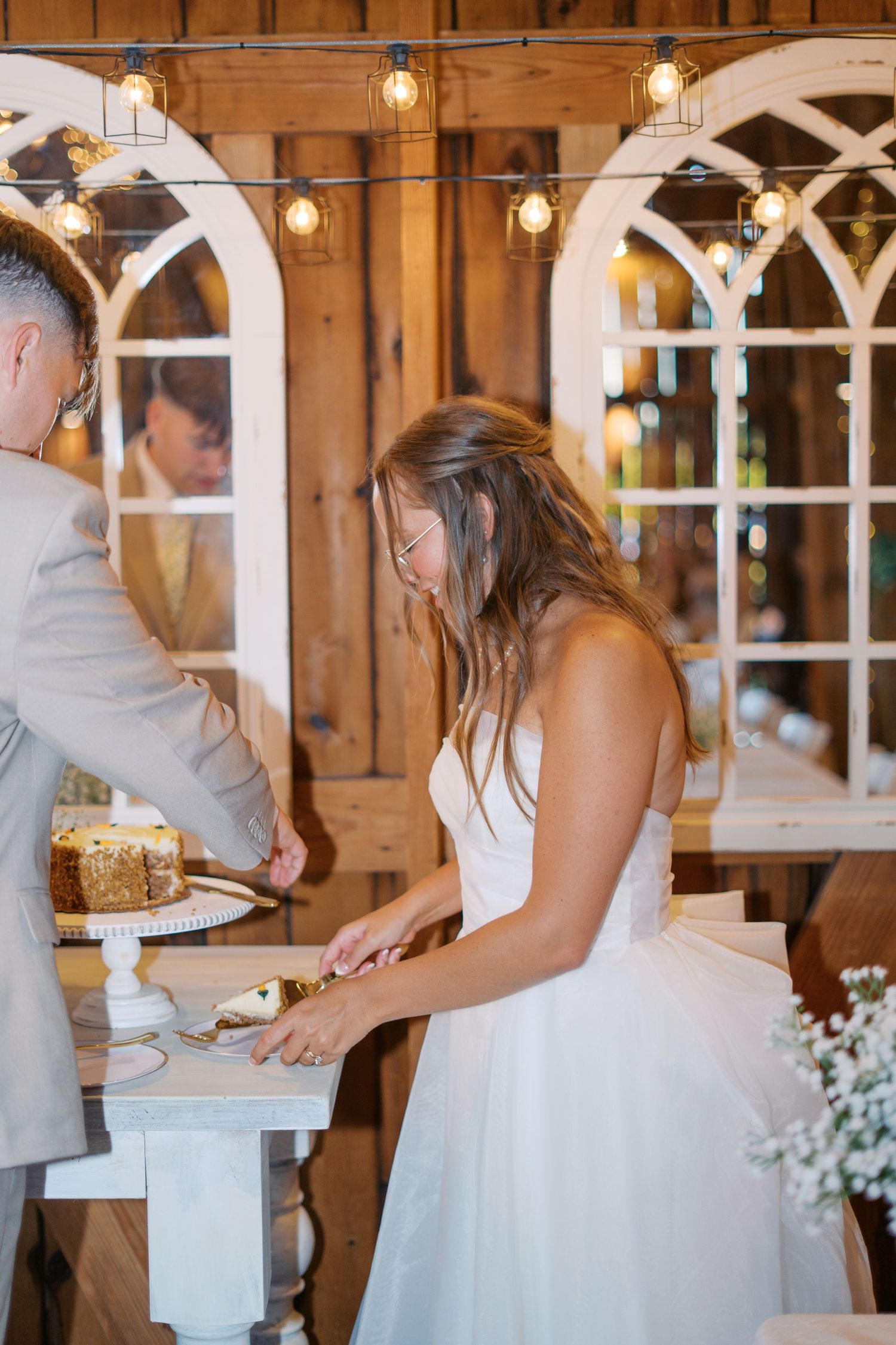 Wedding cake cutting moment in rustic barn venue with decorative window arches.