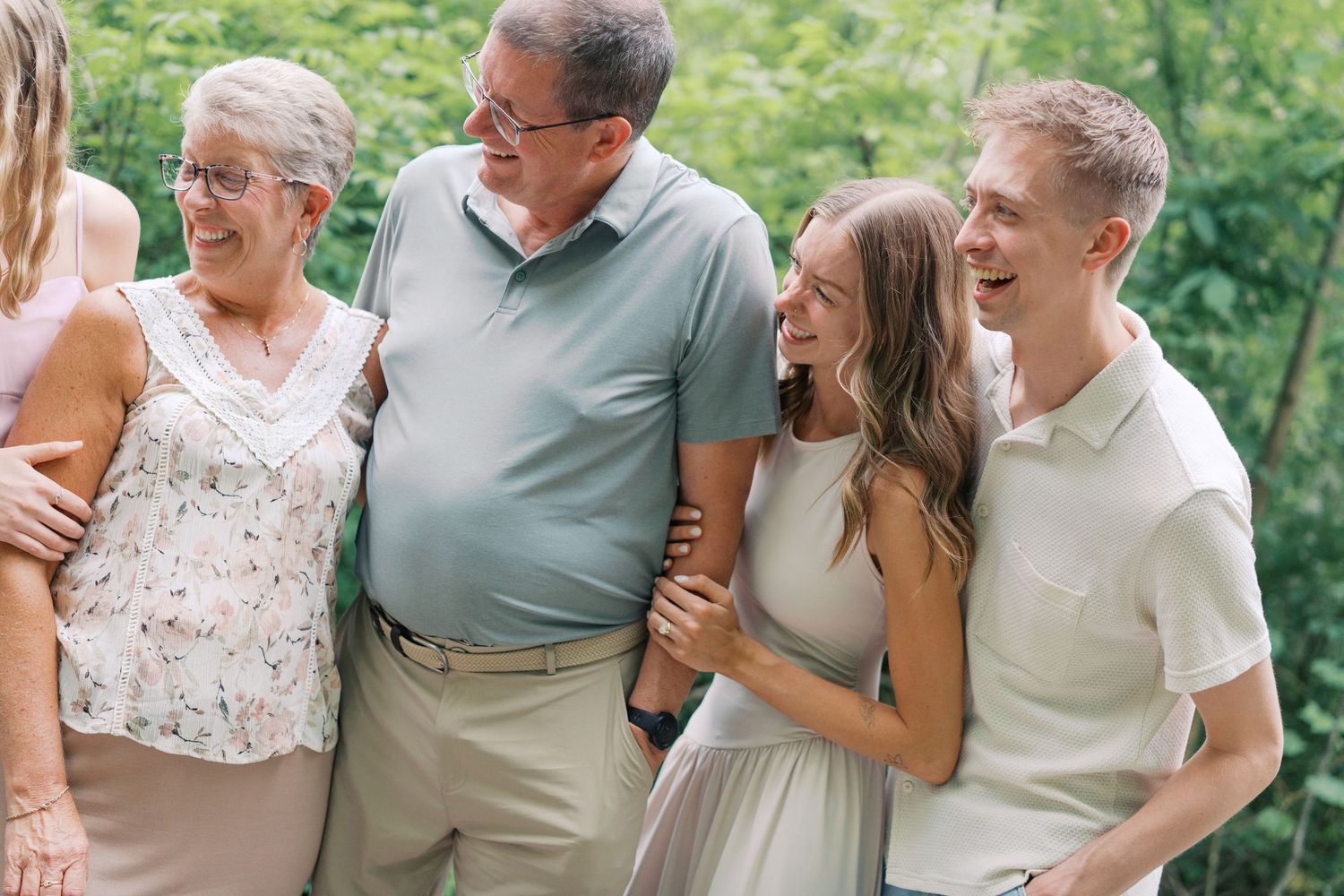 A joyful family group laughing together outdoors, dressed in casual summer attire against a lush green background.