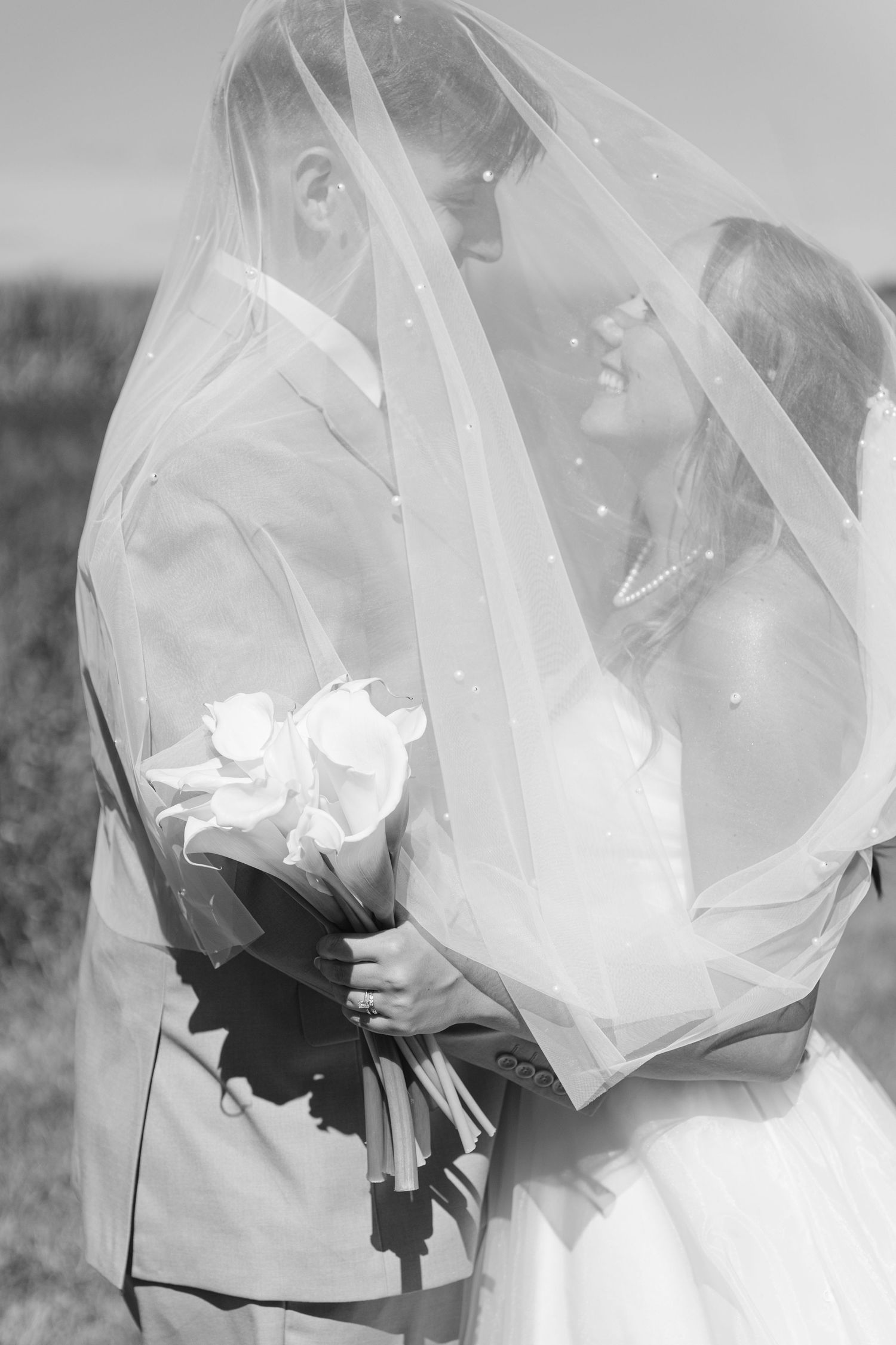 Ethereal black and white portrait of couple beneath flowing wedding veil.