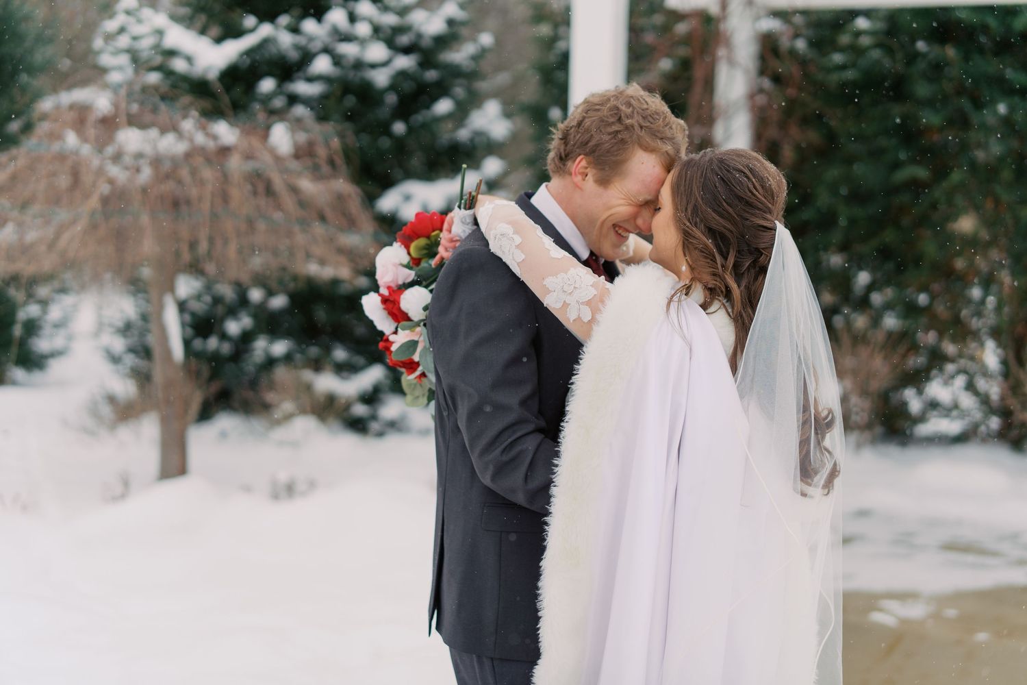 Romantic winter wedding portraits with red floral bouquet in snowy setting.